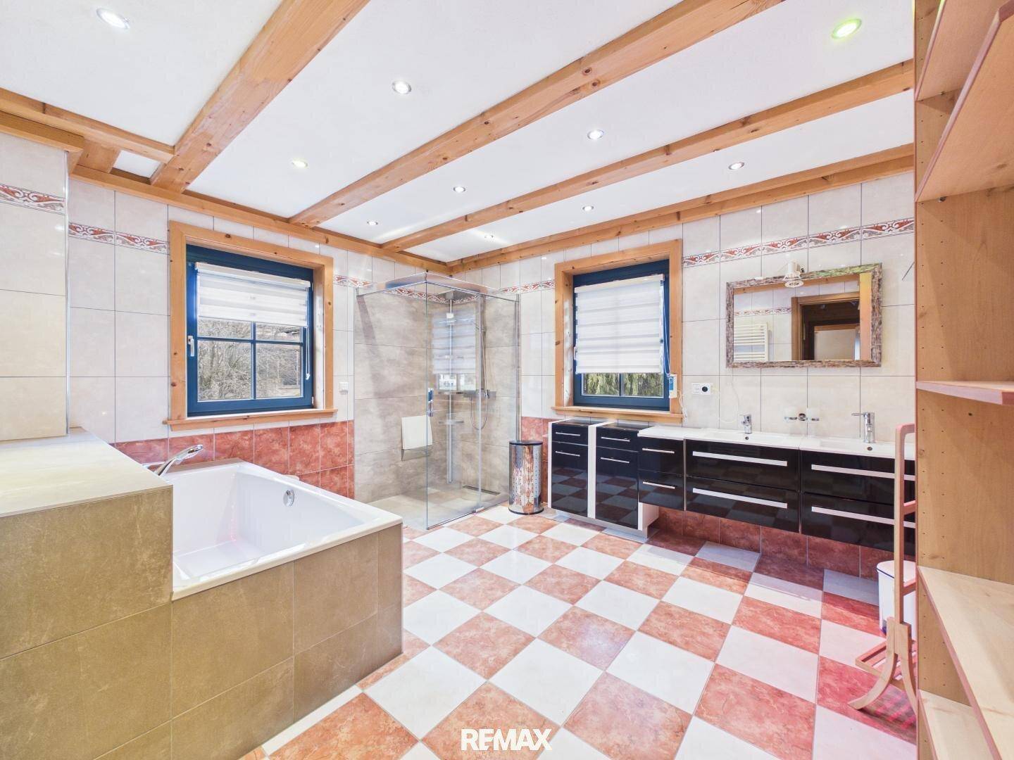 Geräumiges Badezimmer mit Badewanne, großer Dusche, Doppelwaschbecken und Holzbalkendecke.