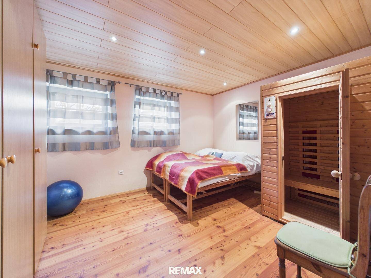 Schlafzimmer mit Holzboden, Holzdecke und integrierter Sauna für private Wellnessmomente.