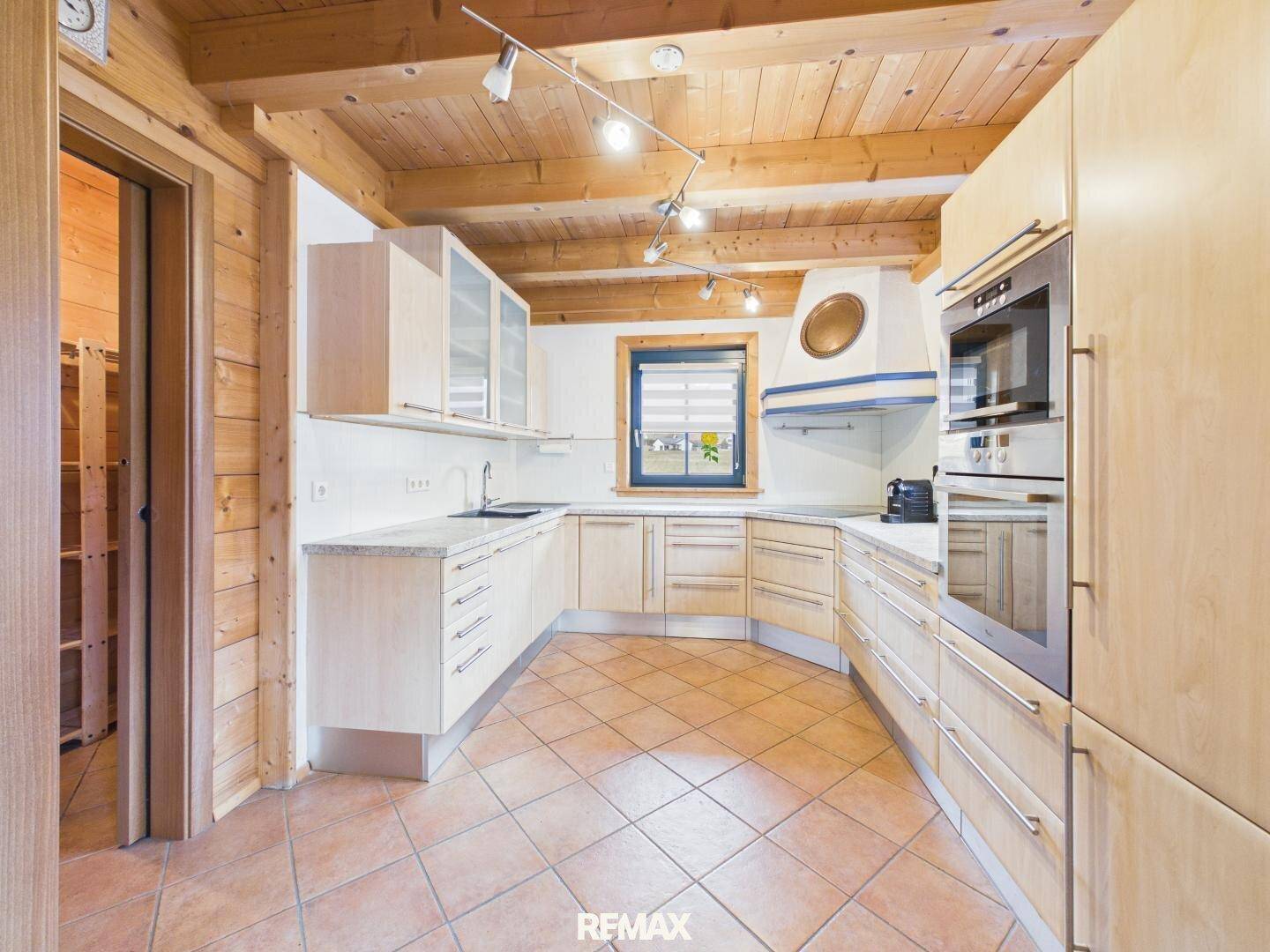 Helle Einbauküche mit Holzschränken, modernen Geräten und Fliesenboden.