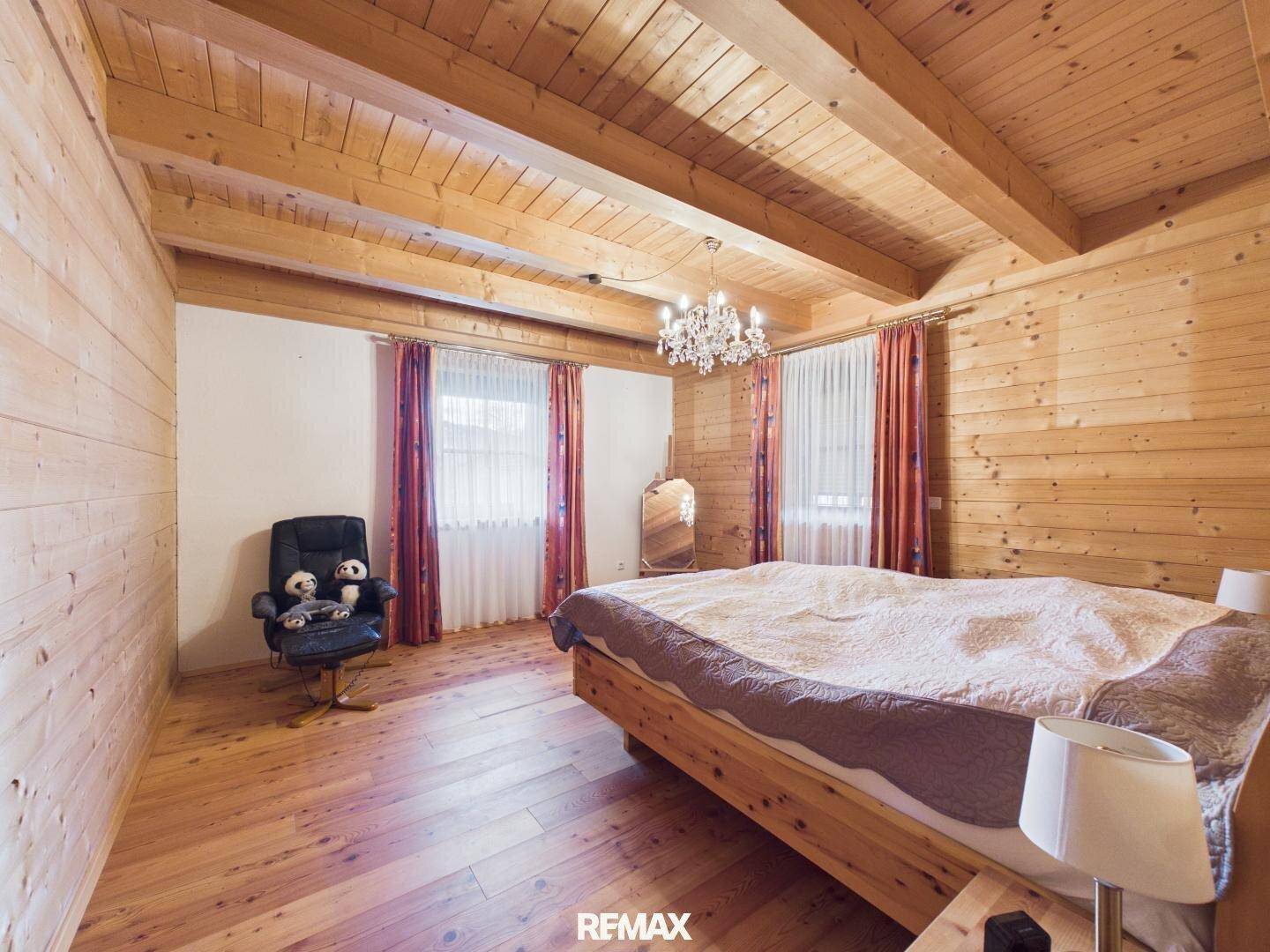 Großes Schlafzimmer mit Holzwänden, Holzbalkendecke und Kronleuchter, bietet viel Platz.