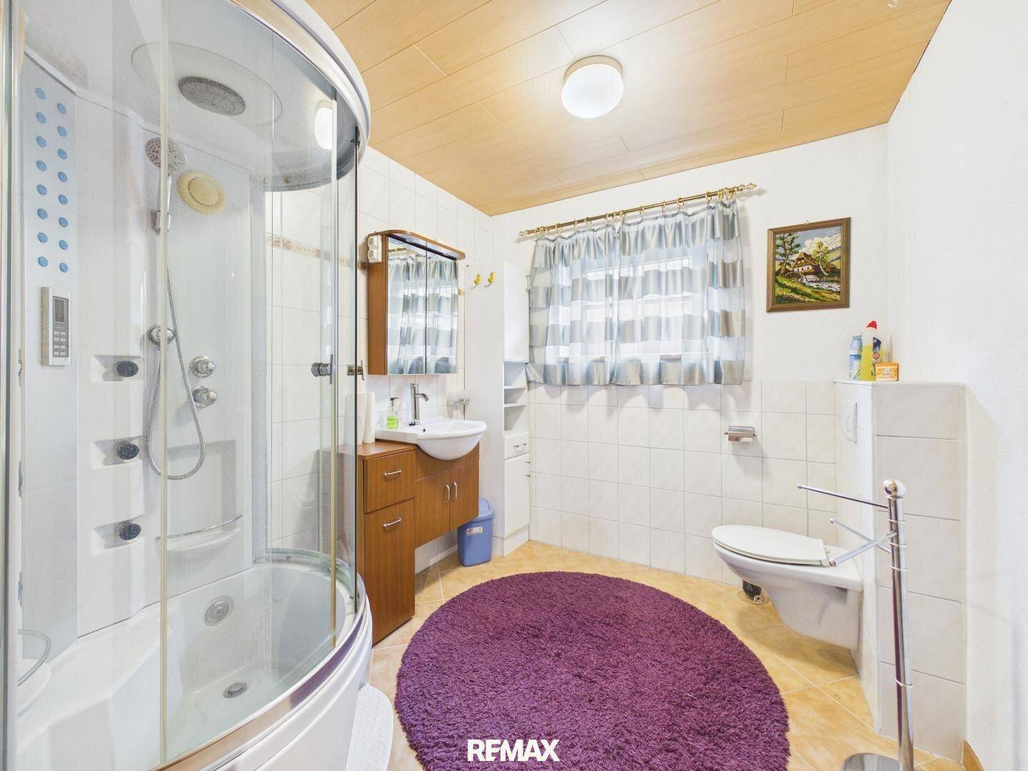 Badezimmer mit Duschkabine, Waschbecken und WC, ausgestattet mit hellen Fliesen und Holzdecke.