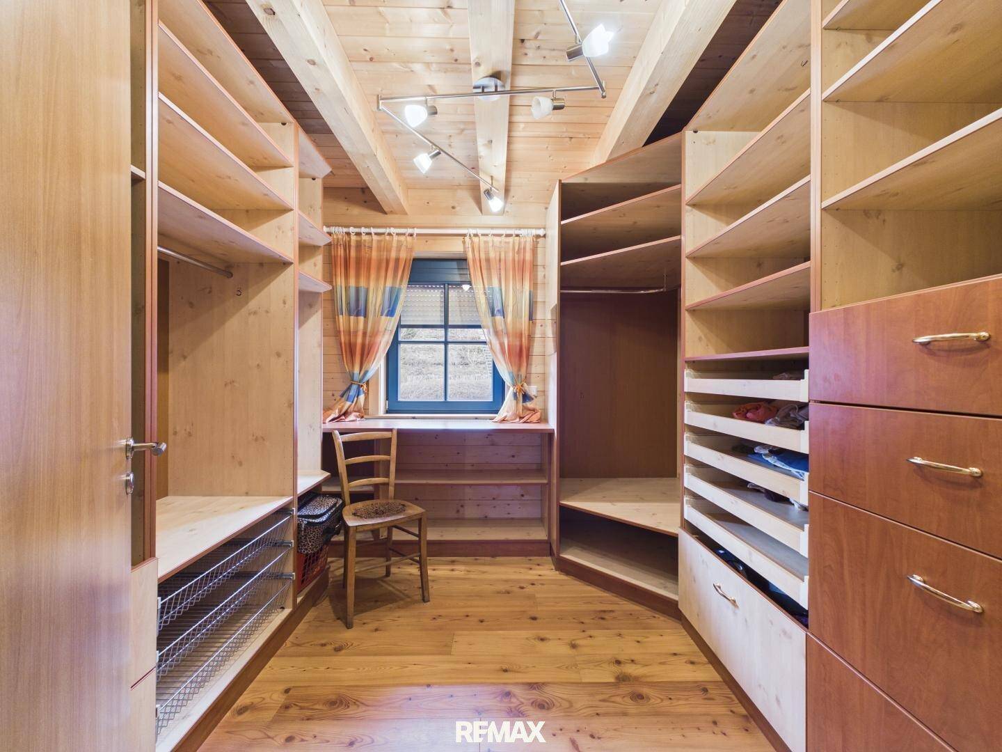 Begehbarer Kleiderschrank mit maßgefertigten Regalen und Holzboden unter einer Holzdecke.