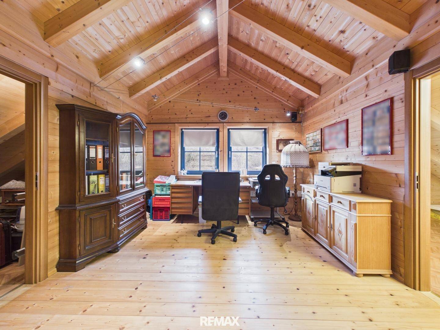 Geräumiges Büro mit Holzwänden, Holzbalkendecke und zwei Fenstern für viel Tageslicht.
