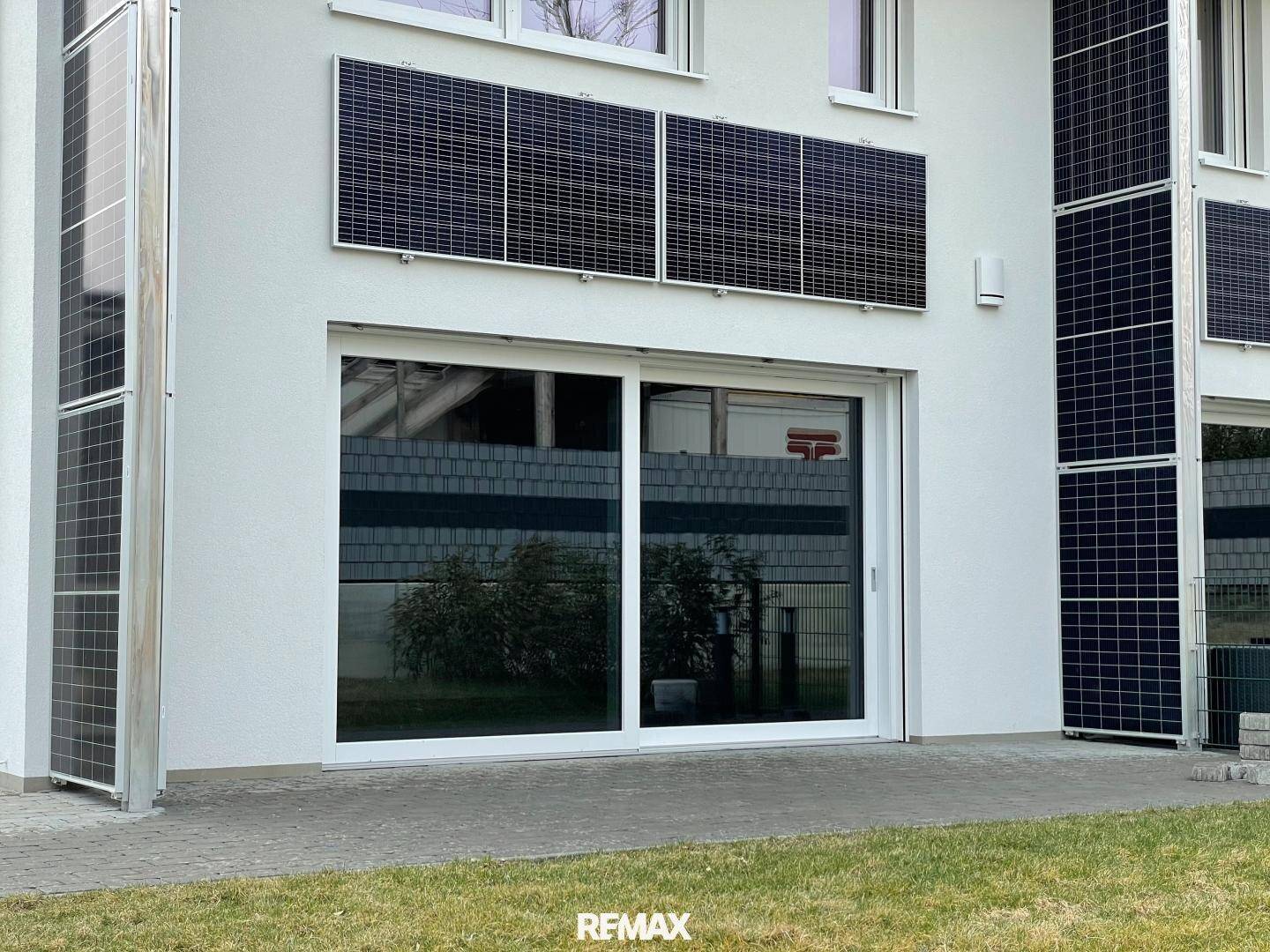 Nahaufnahme der weißen Hausfassade mit großen Schiebetüren und integrierten Solarmodulen.