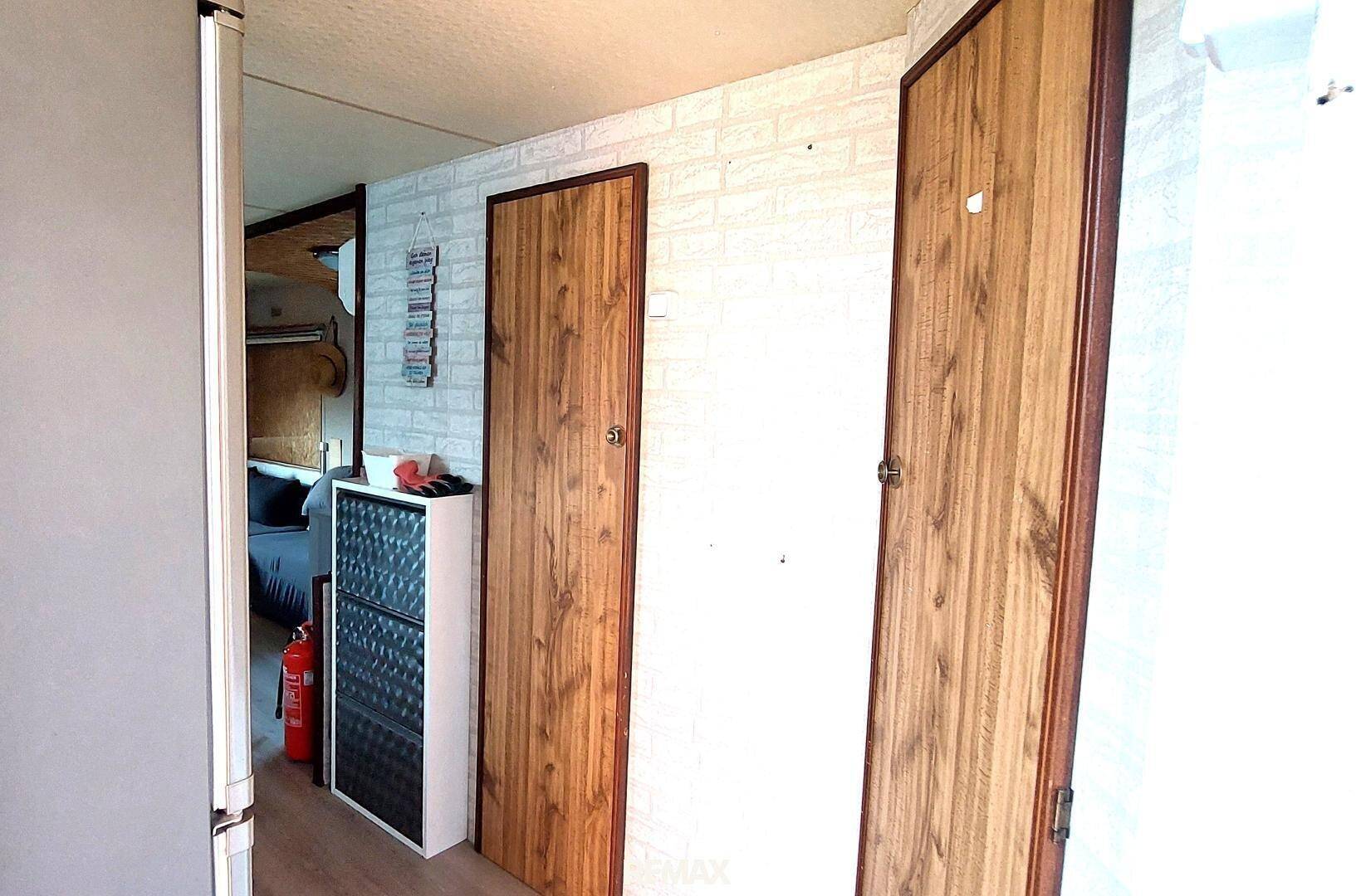 Schmaler Flur mit Holztüren, Schuhschrank und einer Wand mit Ziegelmuster-Tapete.
