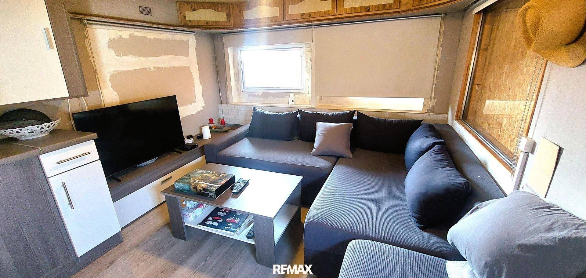 Wohnzimmer mit großem Ecksofa, Couchtisch, Fernseher und Fenstern mit Rollos.
