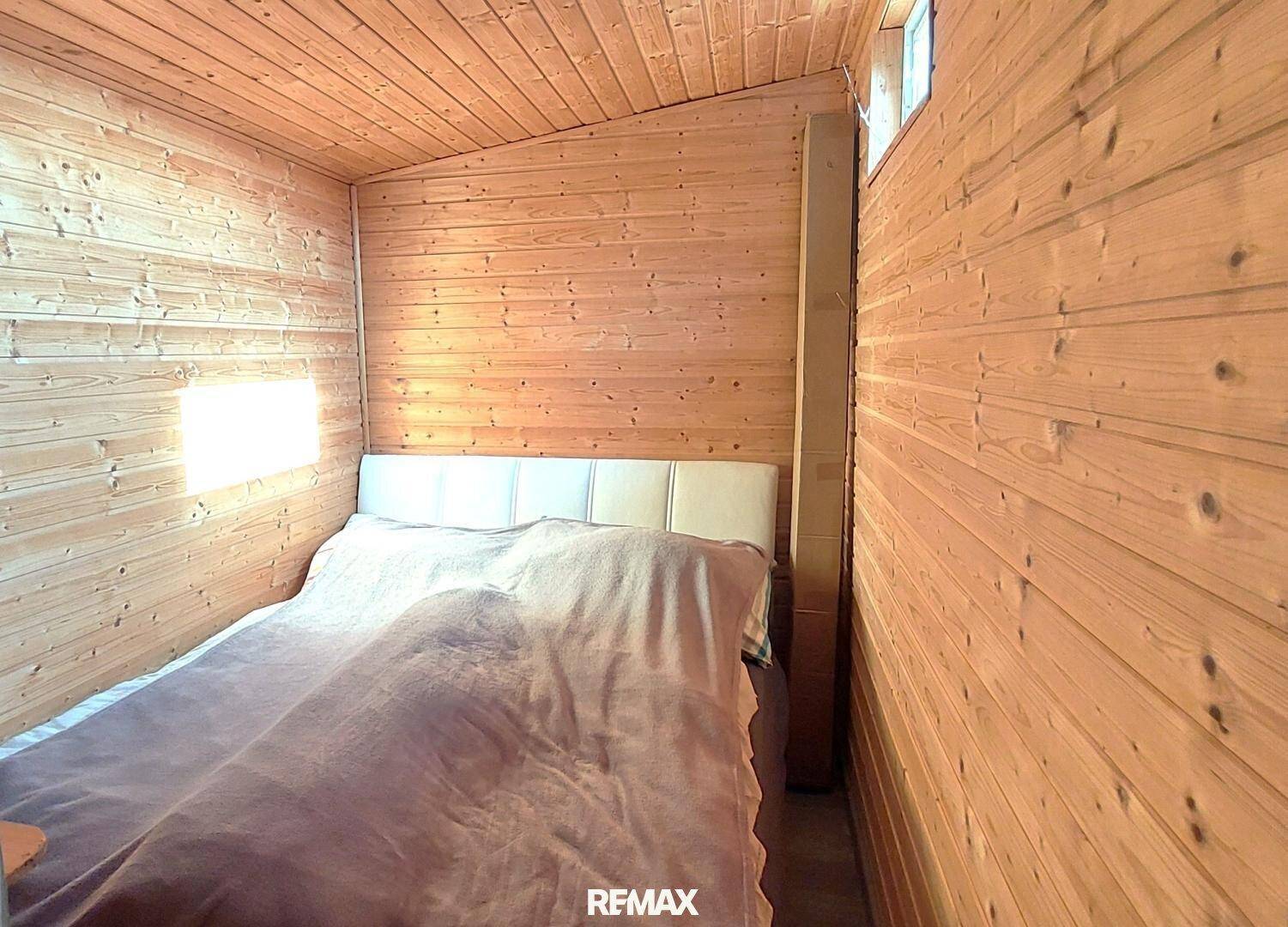 Gemütliches Schlafzimmer mit Holzwänden und -decke, einem Doppelbett und natürlichem Lichteinfall.