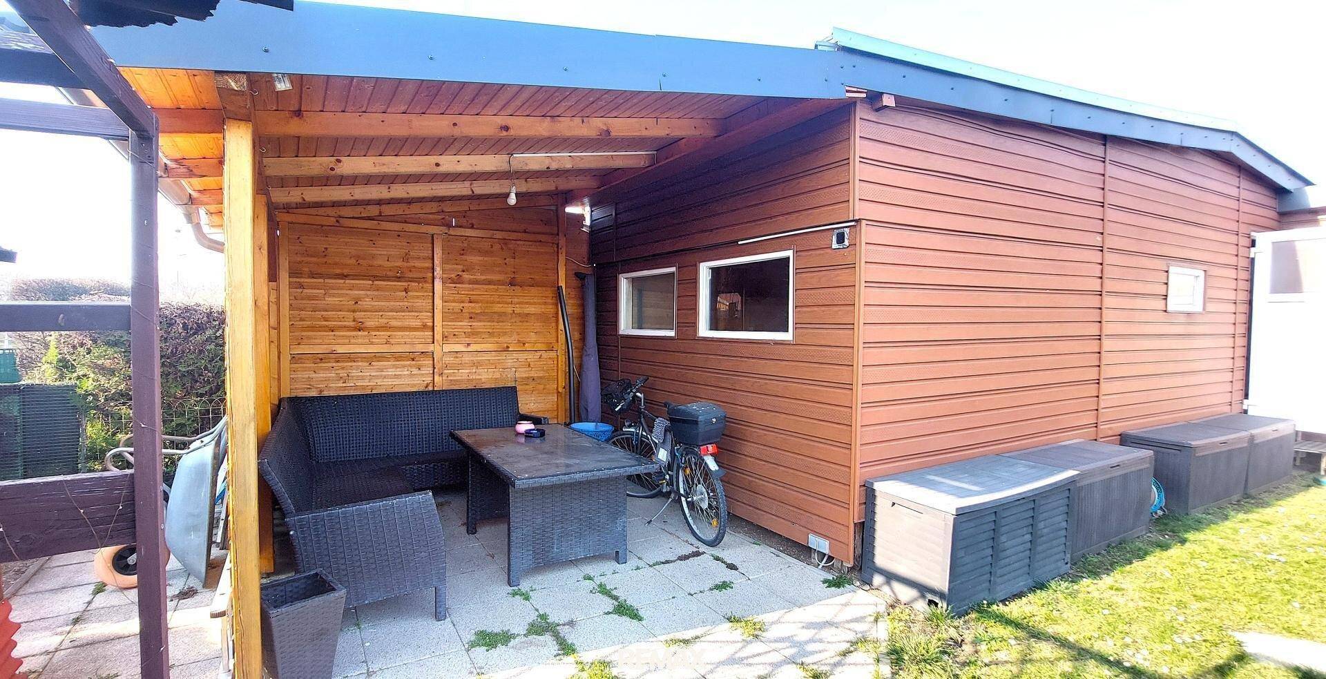 Überdachte Terrasse mit Holzverkleidung, Gartenmöbeln und einem Fahrrad neben dem Haus.