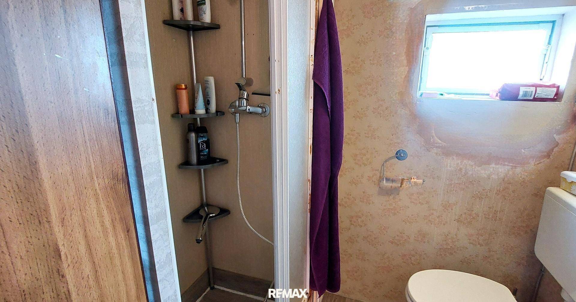 Kleines Badezimmer mit Duschkabine, Toilette und einem Fenster für natürliche Belüftung.