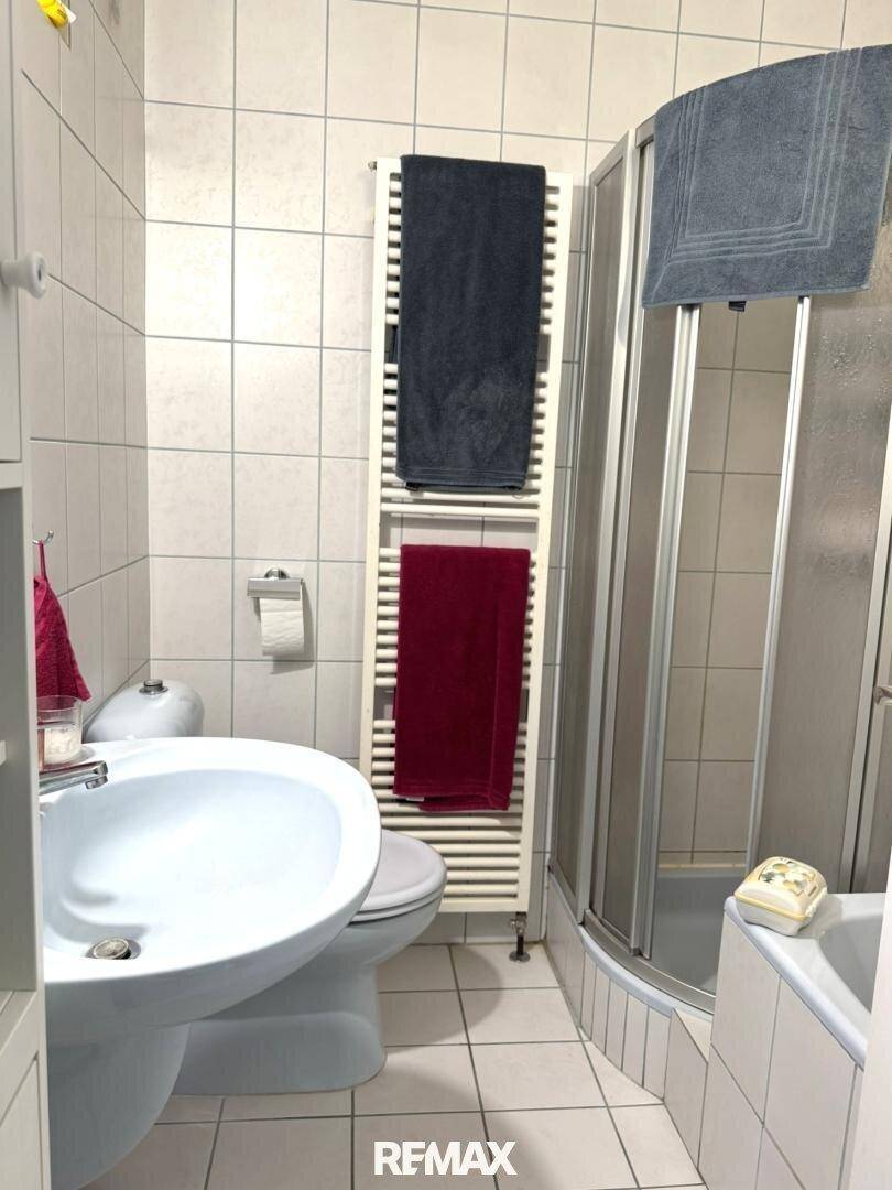 Gefliestes Badezimmer mit Dusche, WC, Waschbecken und beheiztem Handtuchhalter.