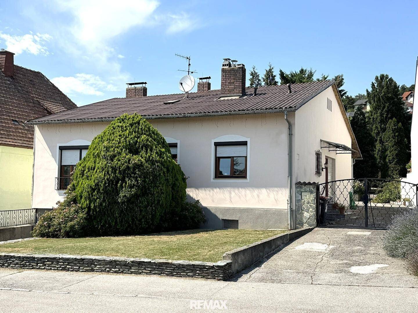 Vorderansicht des Einfamilienhauses mit gepflegtem Vorgarten und Zufahrt unter blauem Himmel.