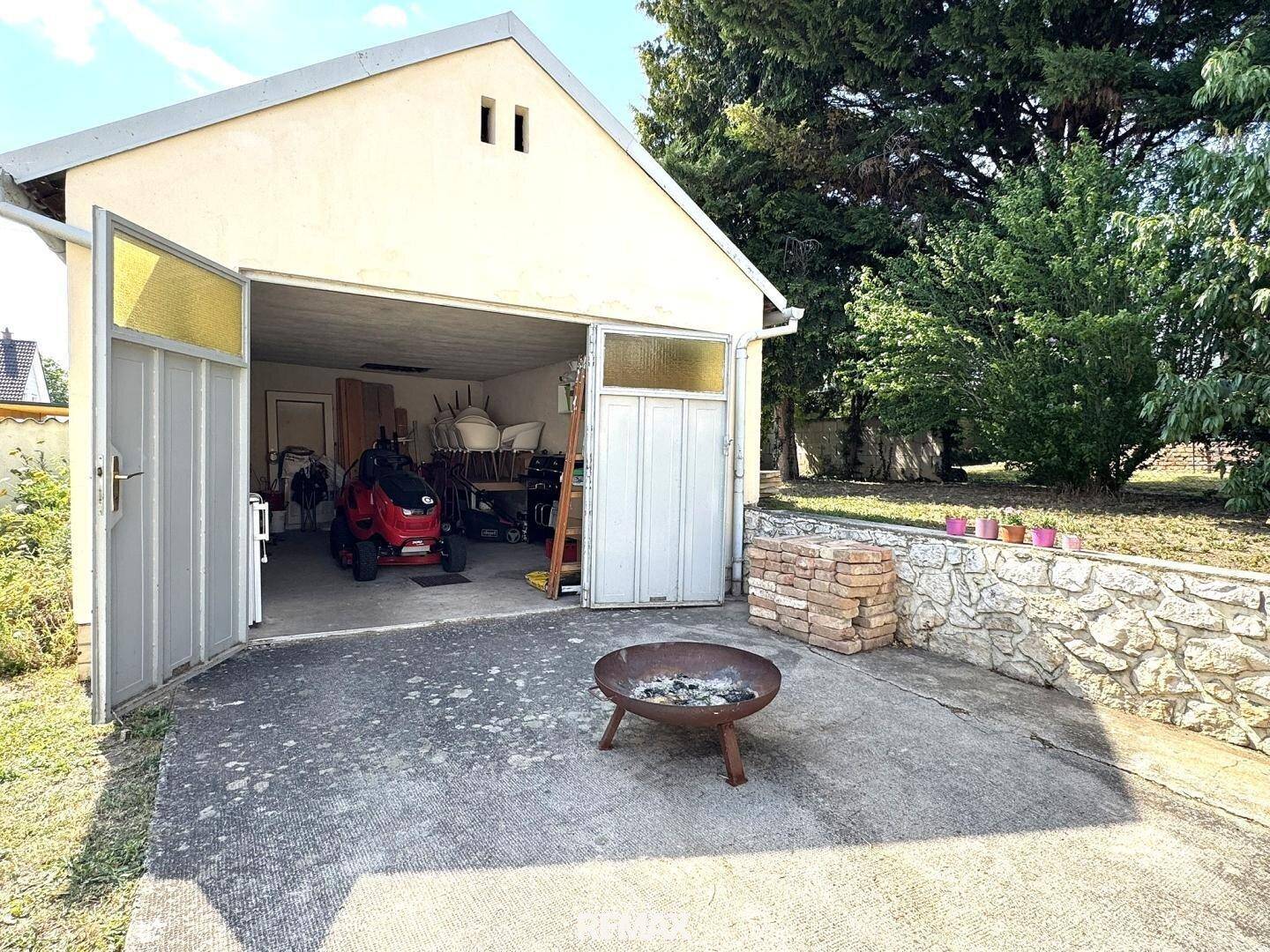 Offene Garage mit Werkzeugen und Geräten, davor eine Feuerstelle auf dem gepflasterten Hof.
