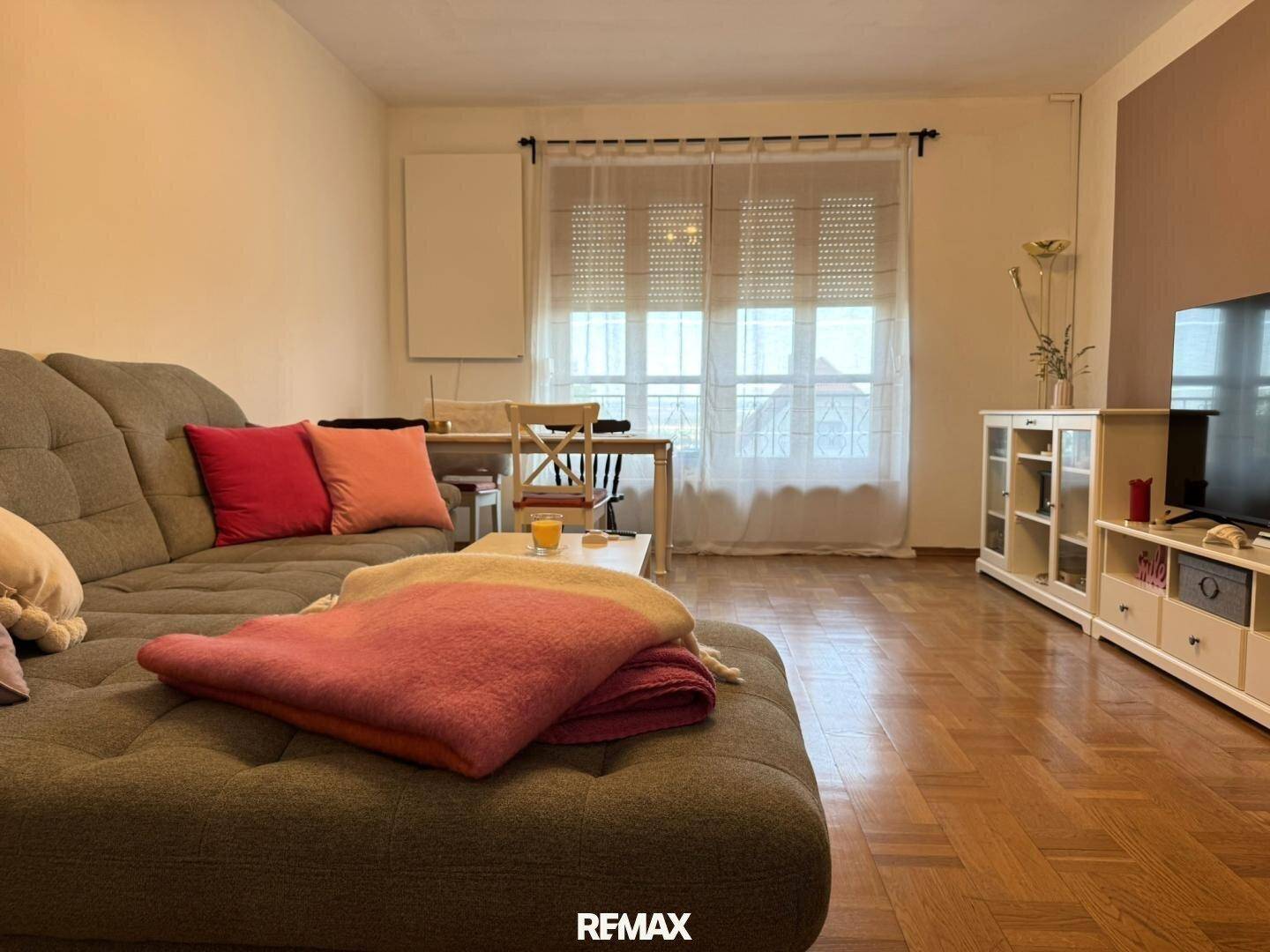 Gemütlicher Wohn- und Essbereich mit Parkettboden, Sofa und Esstisch am Fenster.