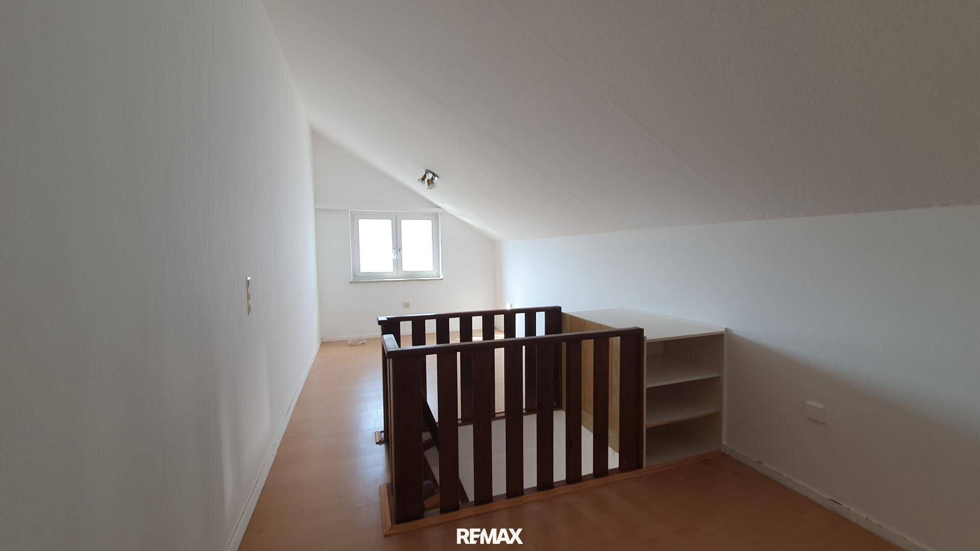 Heller Dachbodenraum mit schrägen Wänden, Laminatboden, Fenster und Holzgeländer.