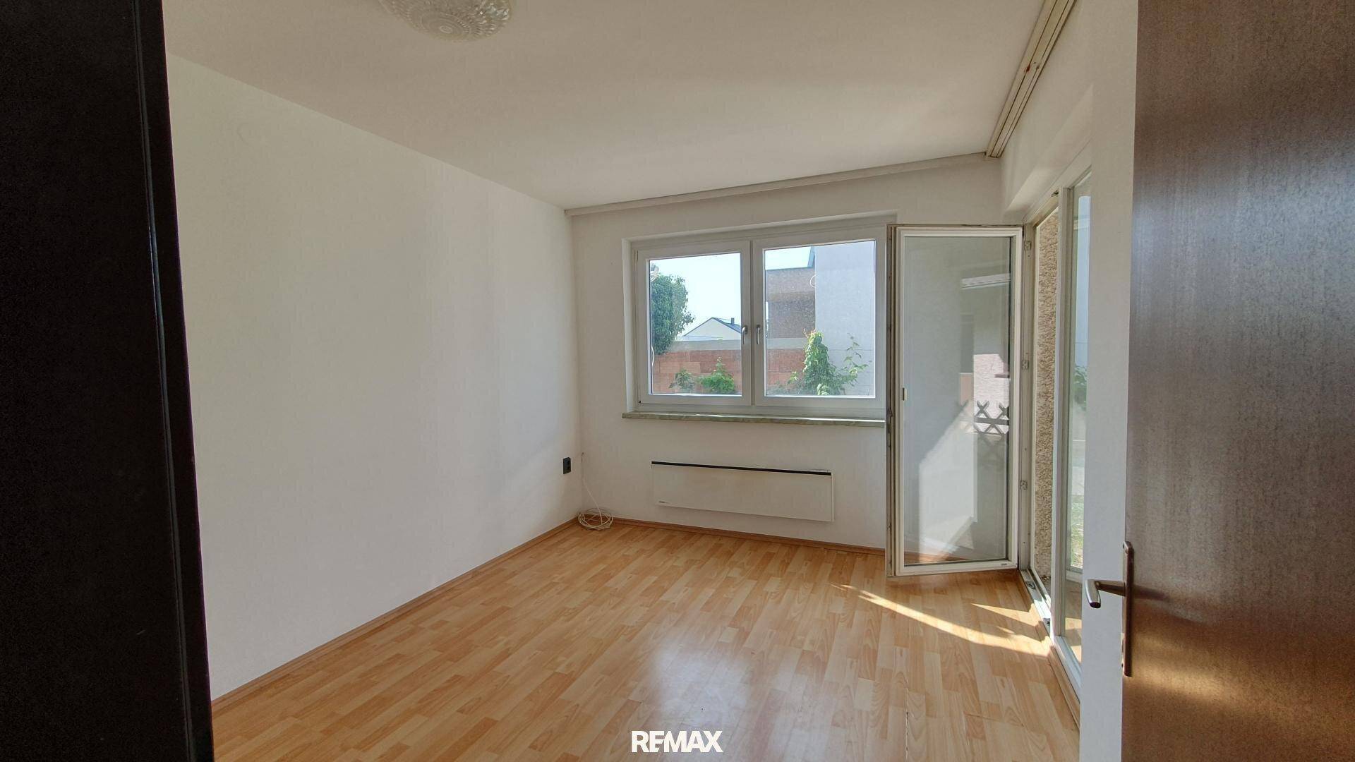 Lichtdurchfluteter Raum mit Laminatboden, großem Fenster und Zugang zu einem Außenbereich.