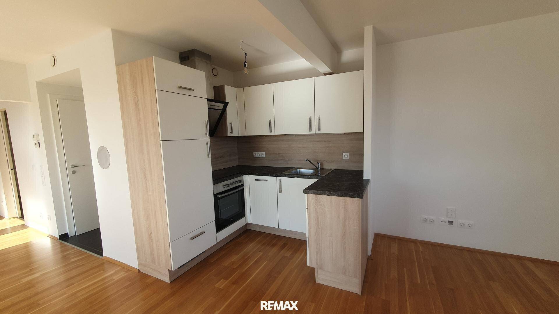Moderne Einbauküche mit hellen Fronten, dunkler Arbeitsplatte und integrierten Geräten.