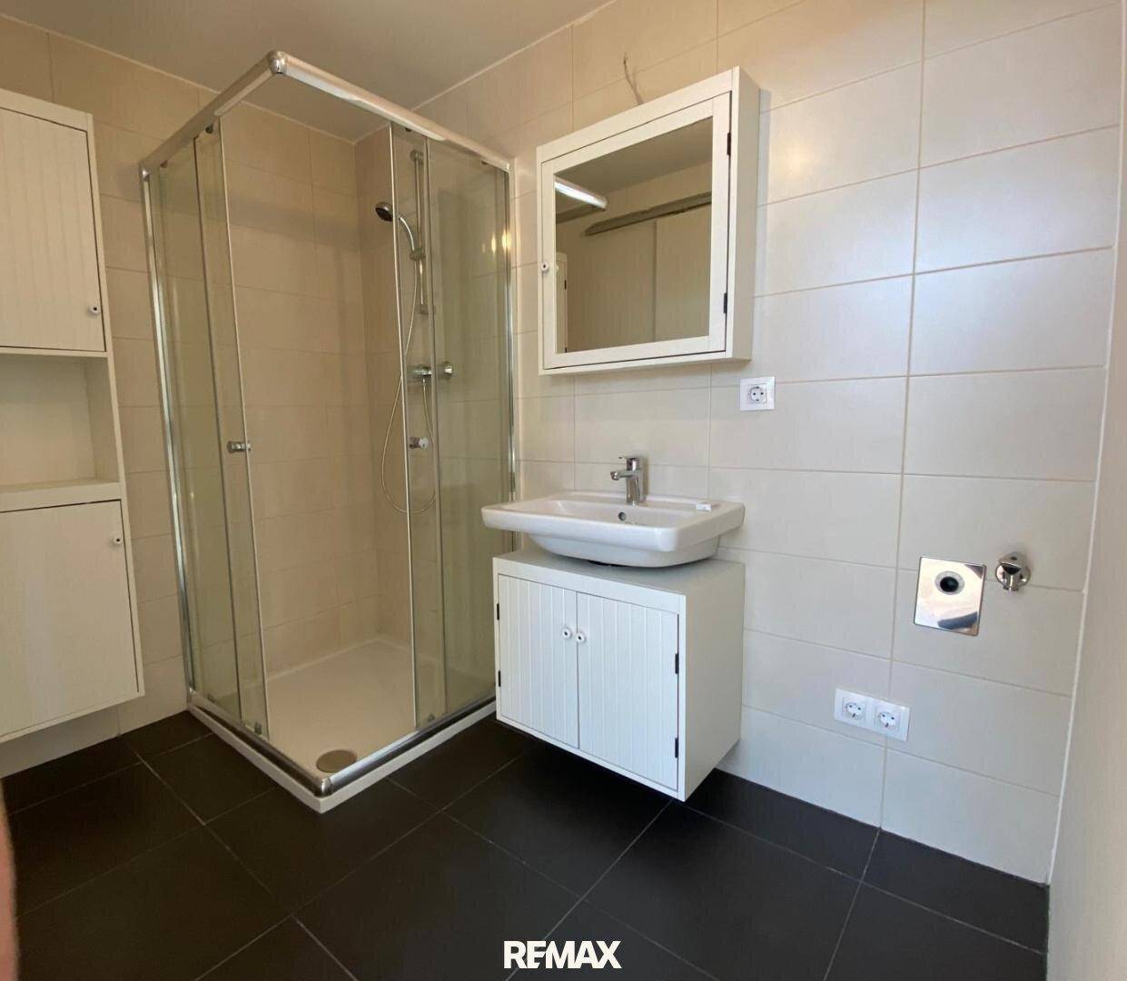 Modernes Badezimmer mit Duschkabine, Waschbecken und hellen Fliesen an den Wänden.