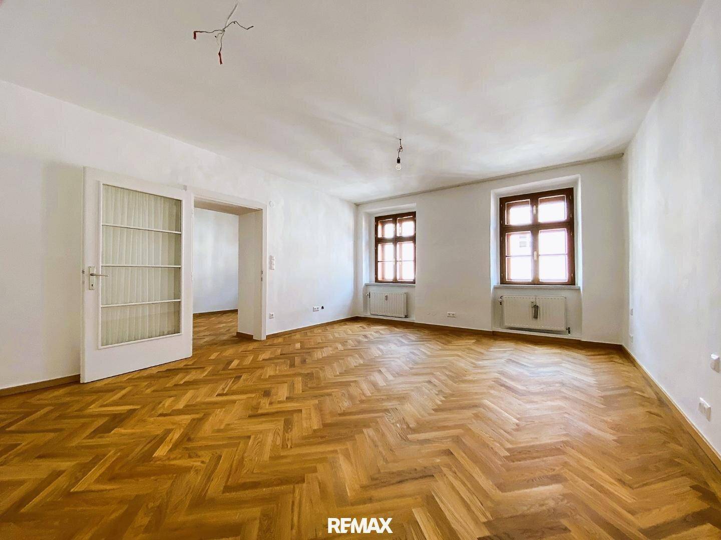 Großes, helles Zimmer mit Fischgrätparkett und einer Doppeltür, ideal für ein Wohn- oder Schlafzimmer.