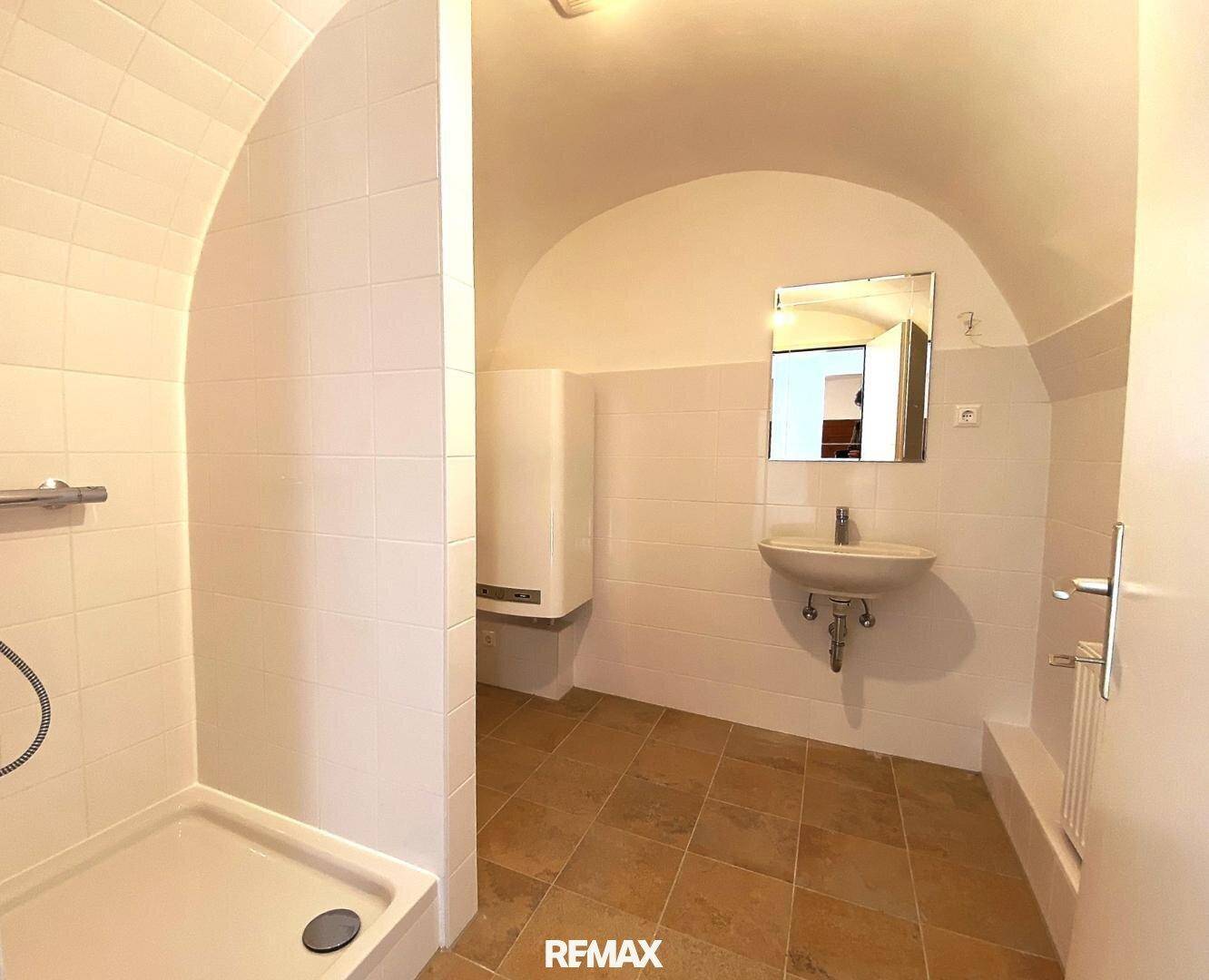 Einfaches Badezimmer mit Dusche, Waschbecken und gewölbter Decke, funktional und hell gefliest.