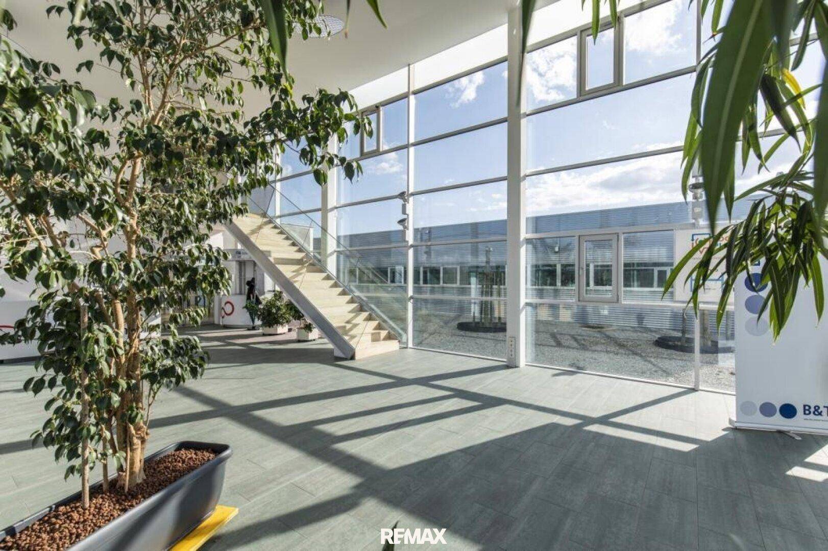 Geräumiger Empfangsbereich mit viel Tageslicht, einer modernen Treppe und Blick nach draußen.