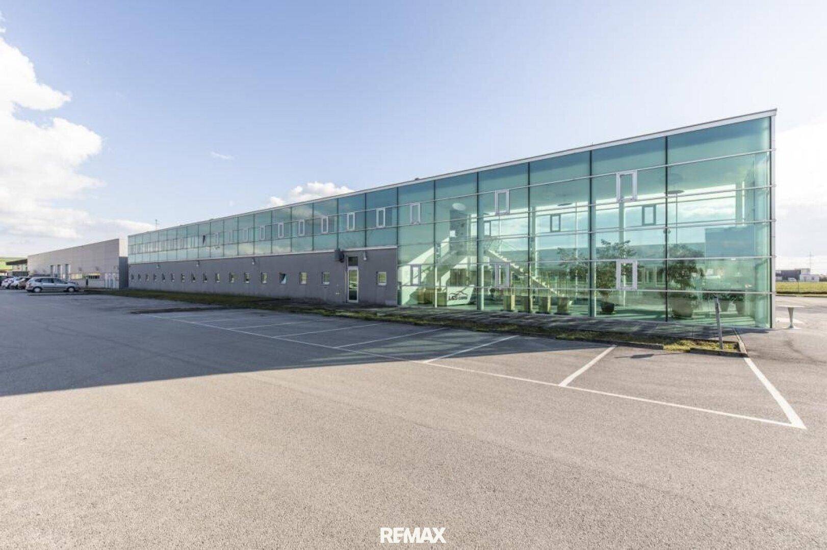 Weitläufige Ansicht des modernen Bürogebäudes mit Glasfront und großem Parkplatzbereich.