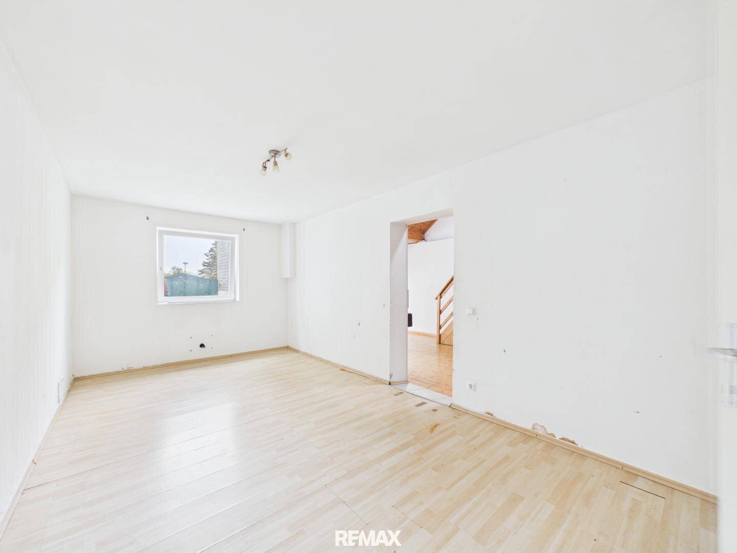 Heller, leerer Raum mit Laminatboden und einem Fenster, das viel Tageslicht hereinlässt.