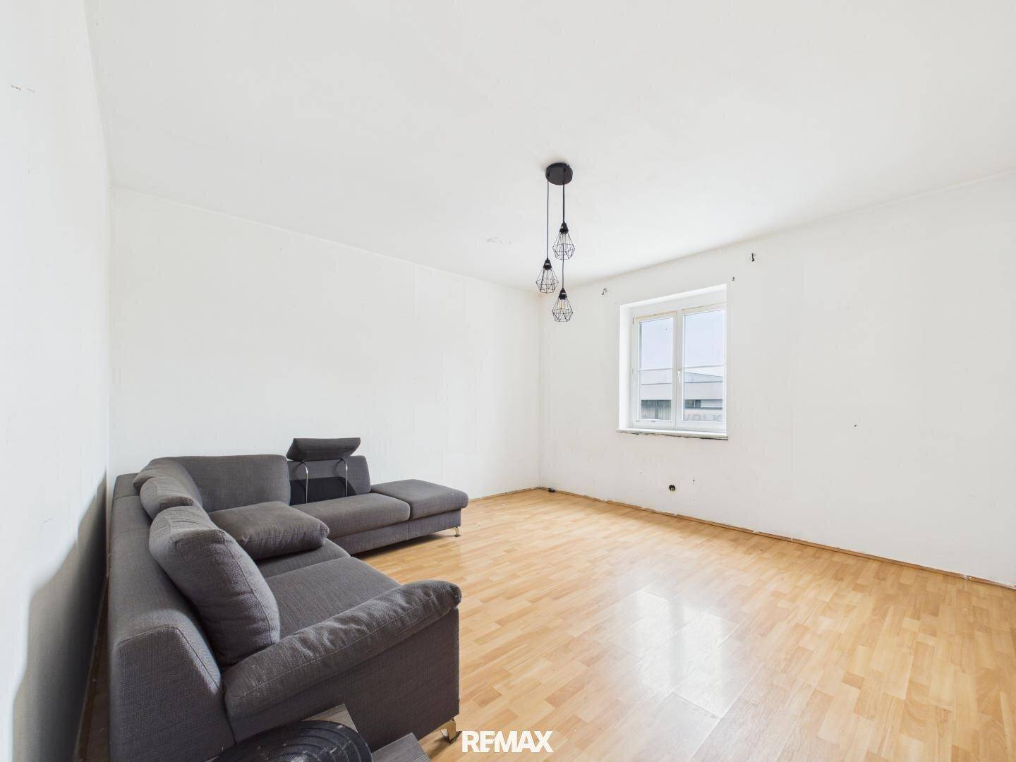 Helles Wohnzimmer mit Laminatboden und einem grauen Ecksofa, bereit zur individuellen Gestaltung.