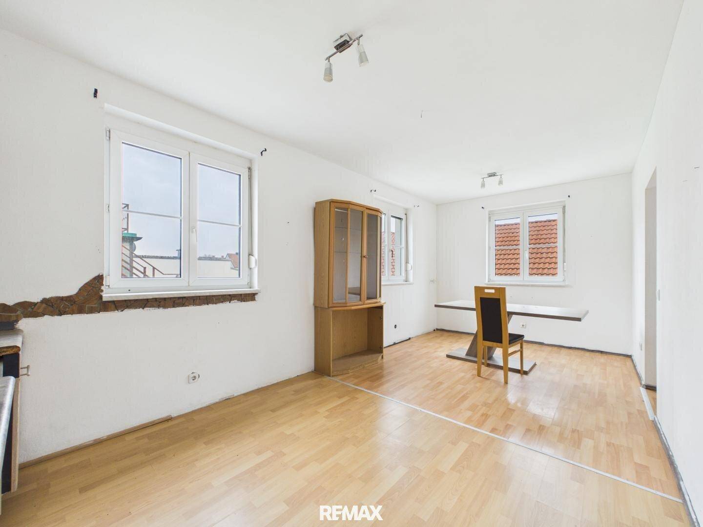 Heller Wohn- und Essbereich mit Laminatboden, großem Fenster und einem Holzschrank.