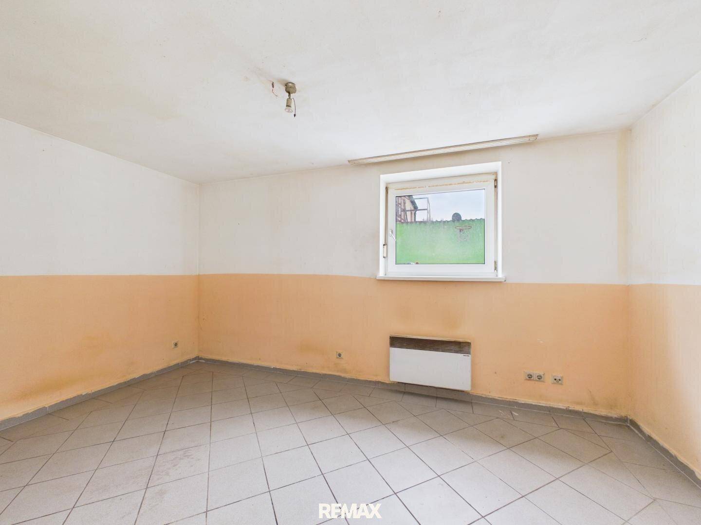 Leerer Raum mit Fliesenboden, zweifarbigen Wänden und einem Fenster mit Blick ins Grüne.