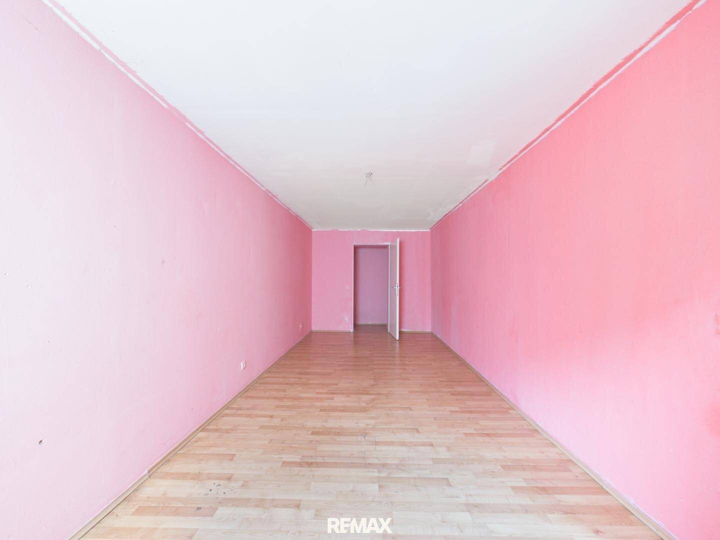 Langer, leerer Raum mit rosa Wänden und Laminatboden, bereit zur individuellen Gestaltung.