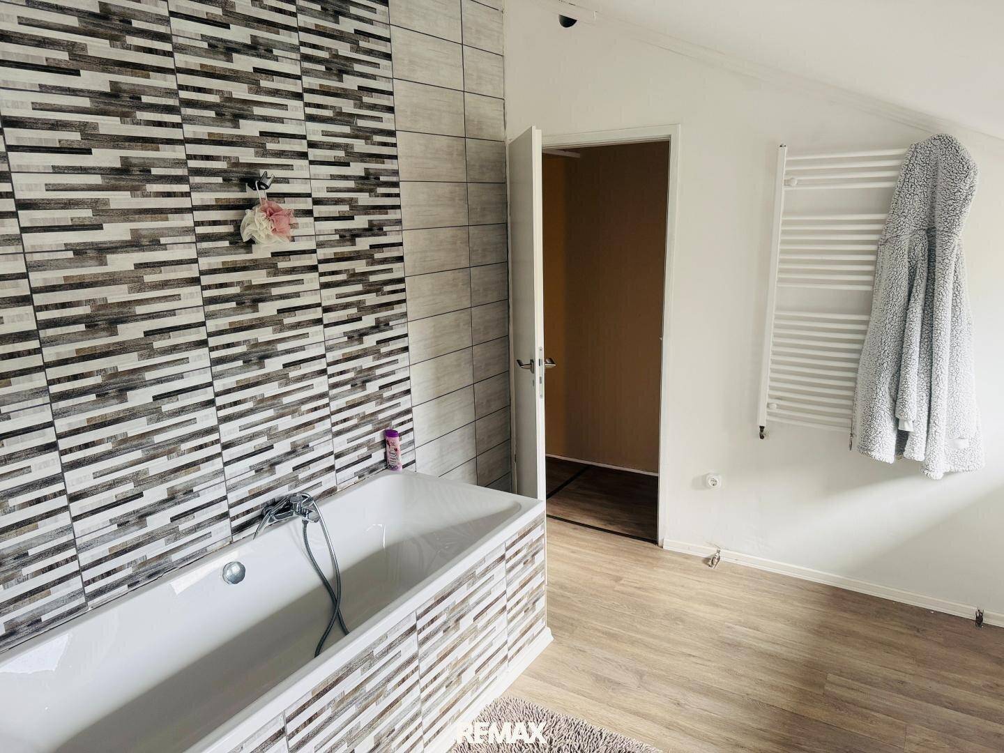 Badezimmer mit Badewanne, gemusterten Fliesen und Handtuchheizkörper.