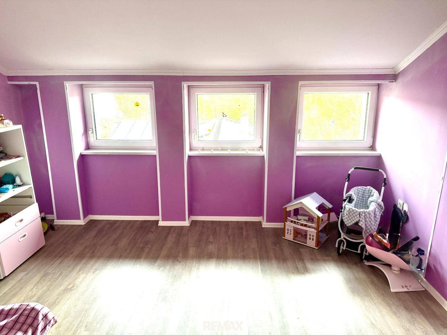 Kinderzimmer mit lila Wänden, drei Fenstern und viel Platz zum Spielen.