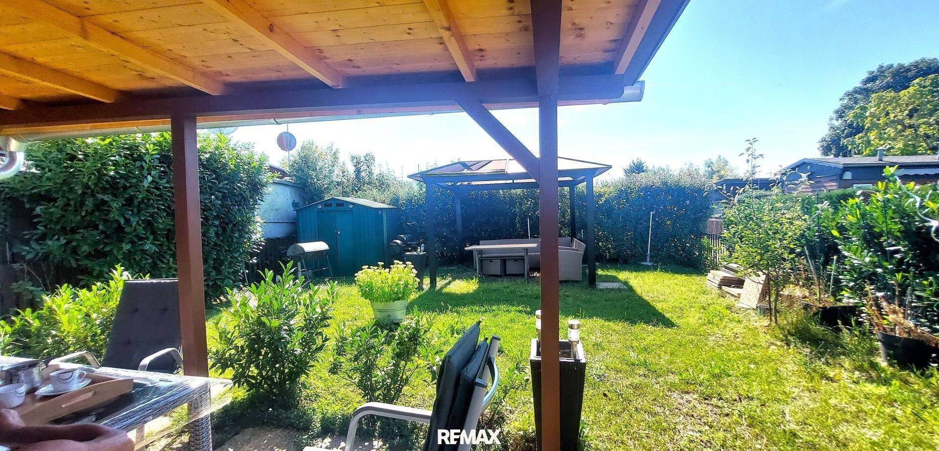 Überdachte Holzterrasse mit Blick auf den Garten, einen Geräteschuppen und eine weitere Sitzecke.