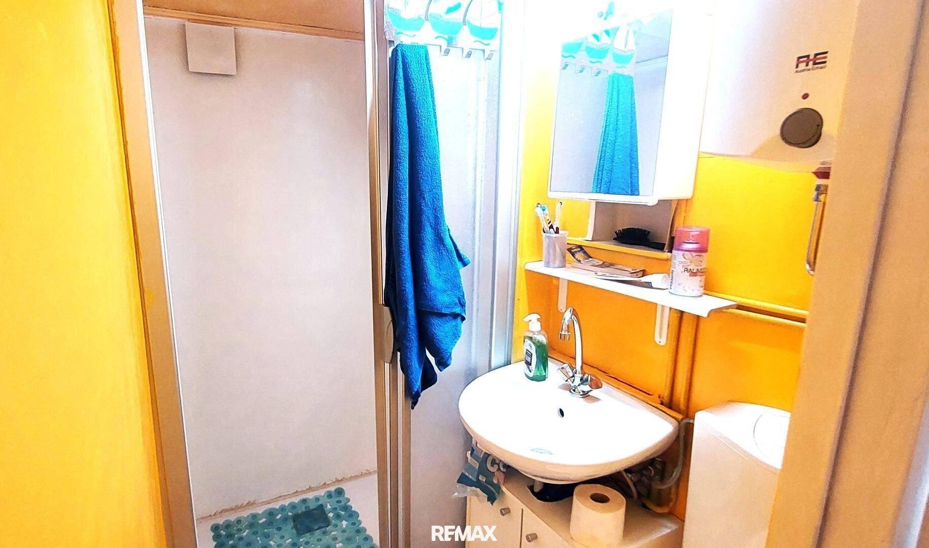 Kleines Badezimmer mit Dusche, Waschbecken und Warmwasserbereiter, gestaltet in leuchtendem Gelb.