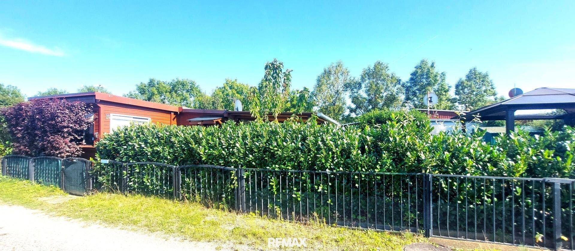 Weitläufige Außenansicht des Anwesens mit Hecke, Zaun und dem kleinen Gebäude im Hintergrund.