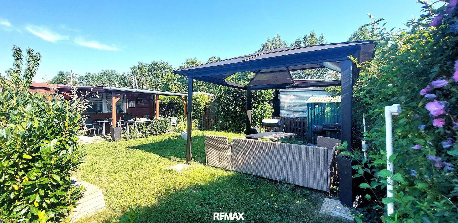 Gepflegter Garten mit Rasenfläche, einer überdachten Lounge-Ecke und dem Hauptgebäude im Hintergrund.
