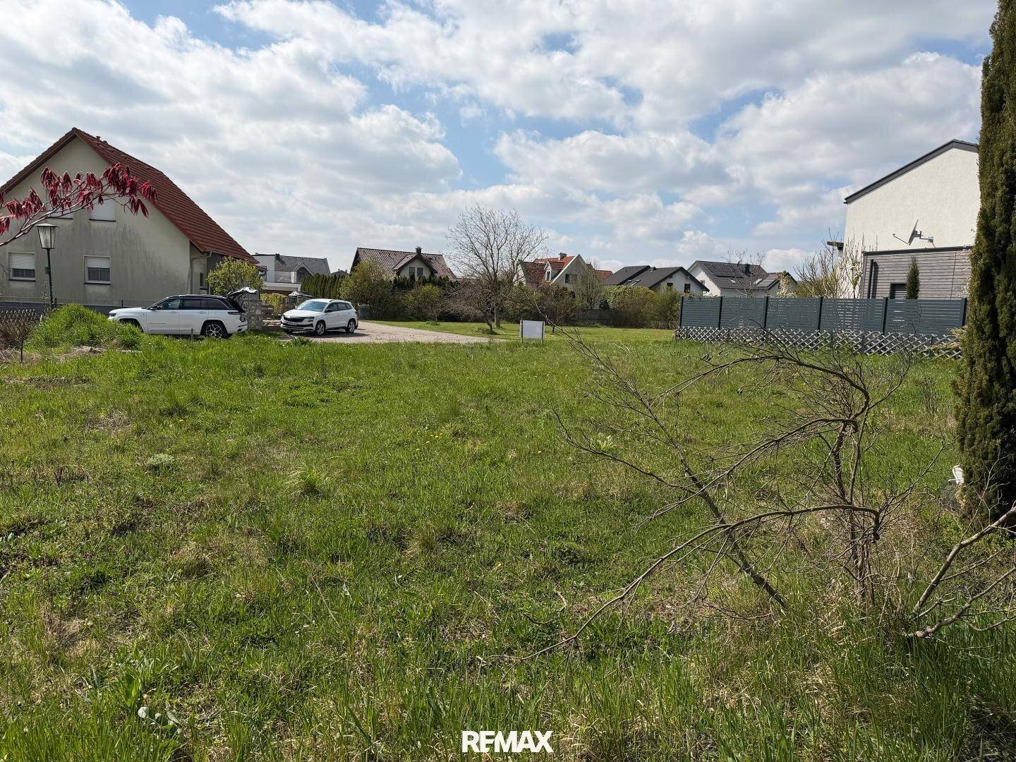 Offenes Grundstück mit Grasfläche, umgeben von Wohnhäusern und parkenden Autos in der Ferne.