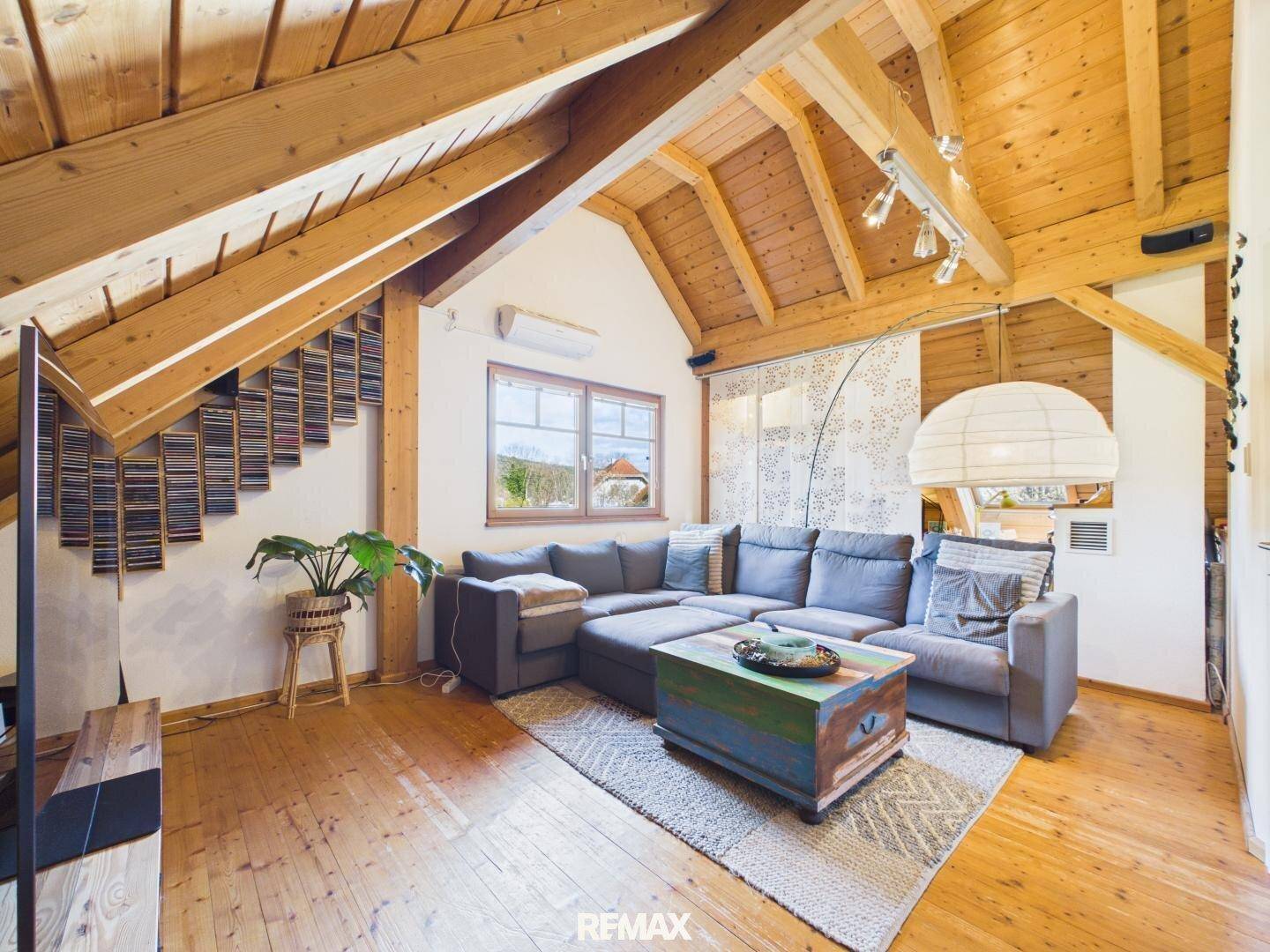 Gemütliches Wohnzimmer mit großem Ecksofa, Holzbalkendecke und Blick ins Grüne.