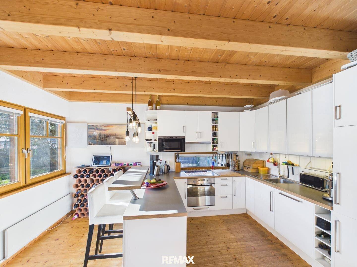 Helle, moderne Küche mit weißen Schränken, Kücheninsel und sichtbaren Holzbalken an der Decke.