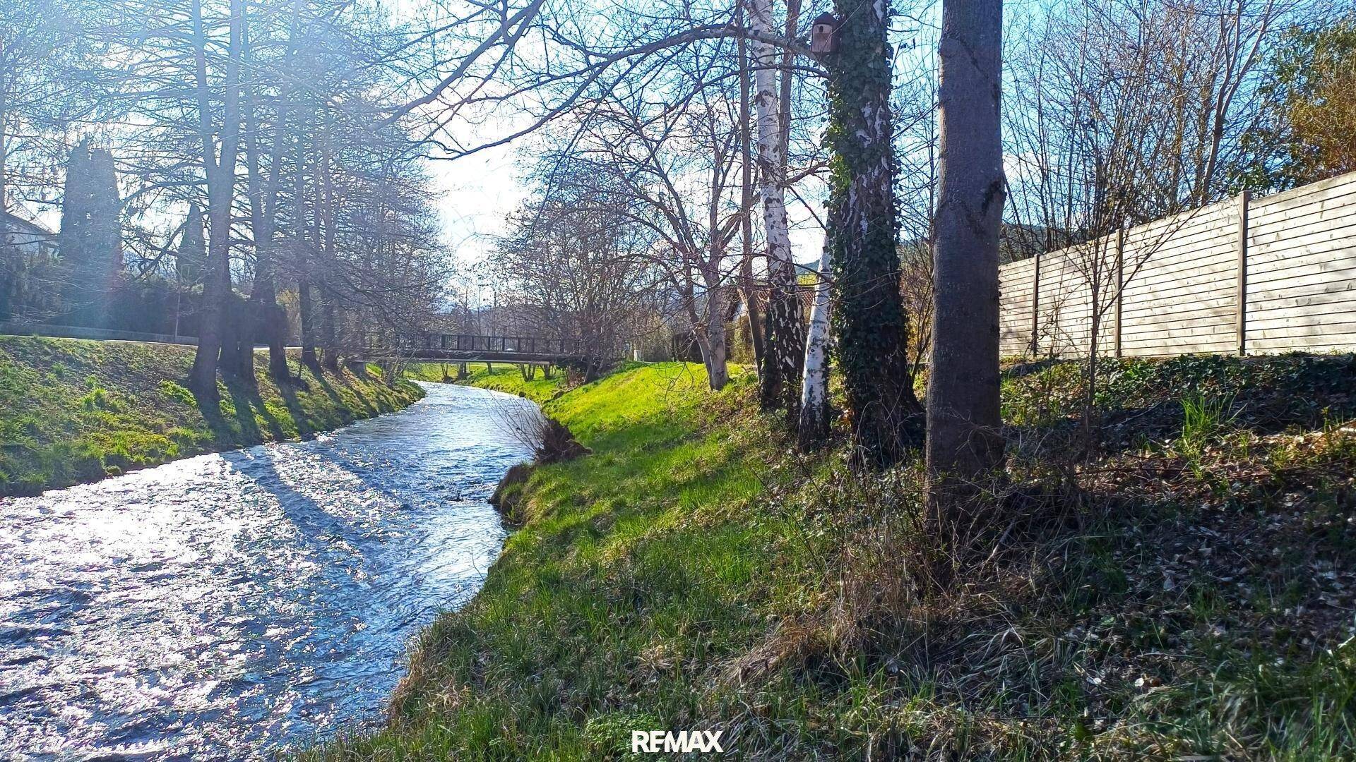 Idyllischer Flusslauf mit grünen Ufern und Bäumen unter strahlend blauem Himmel.