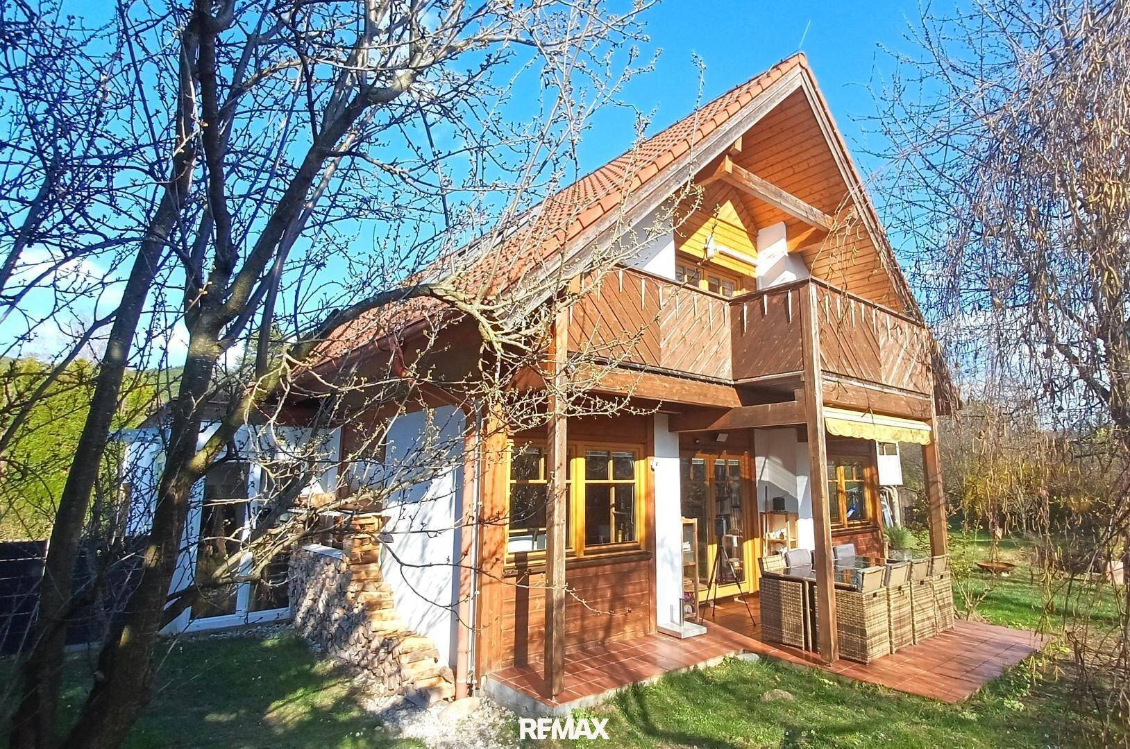 Charmantes Holzhaus mit Balkon und überdachter Terrasse, umgeben von einem gepflegten Garten.