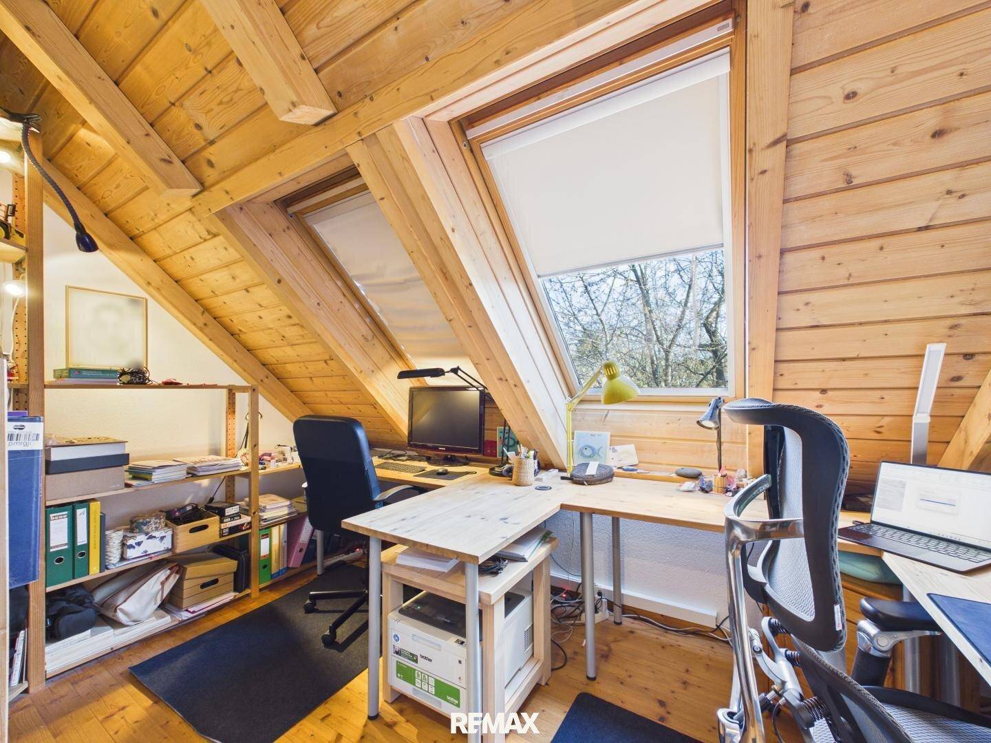 Helles Dachgeschoss-Büro mit Holzverkleidung, Schreibtischen und großen Dachfenstern.