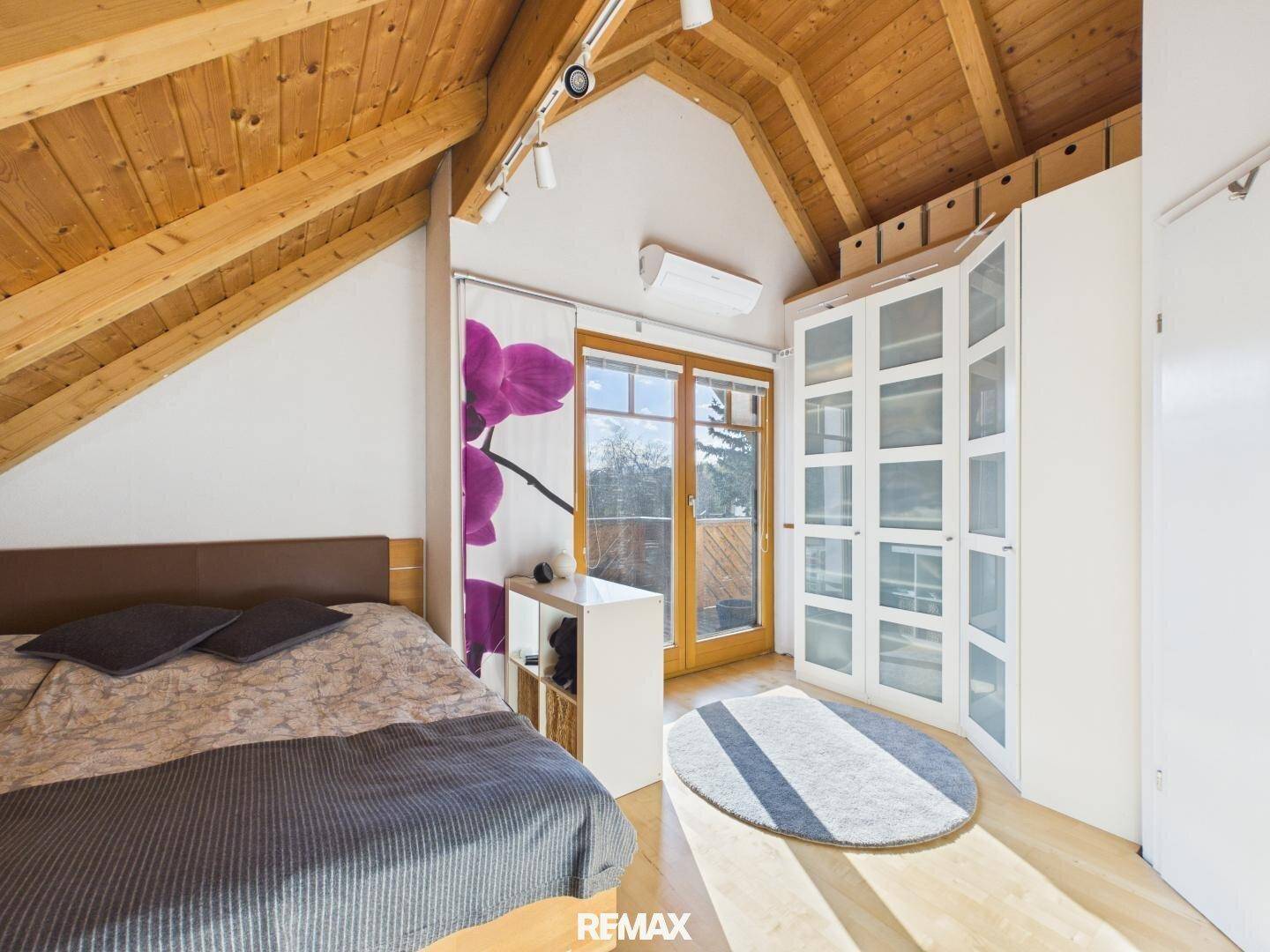Schlafzimmer im Dachgeschoss mit Schrägdach, Kleiderschrank und Zugang zu einem Balkon.