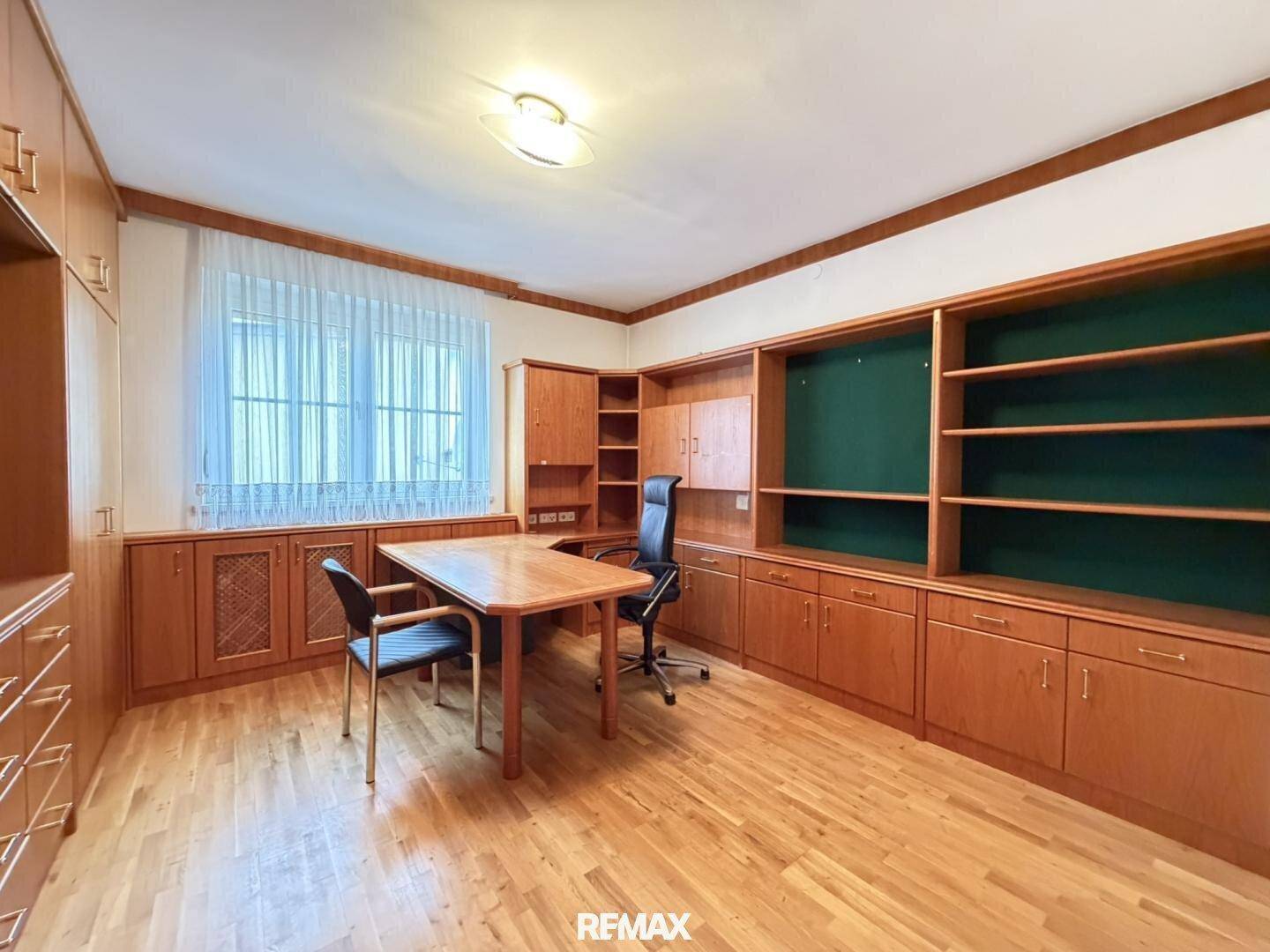 Großes Arbeitszimmer mit umfangreichen Holzregalen, Schreibtisch und Parkettboden.