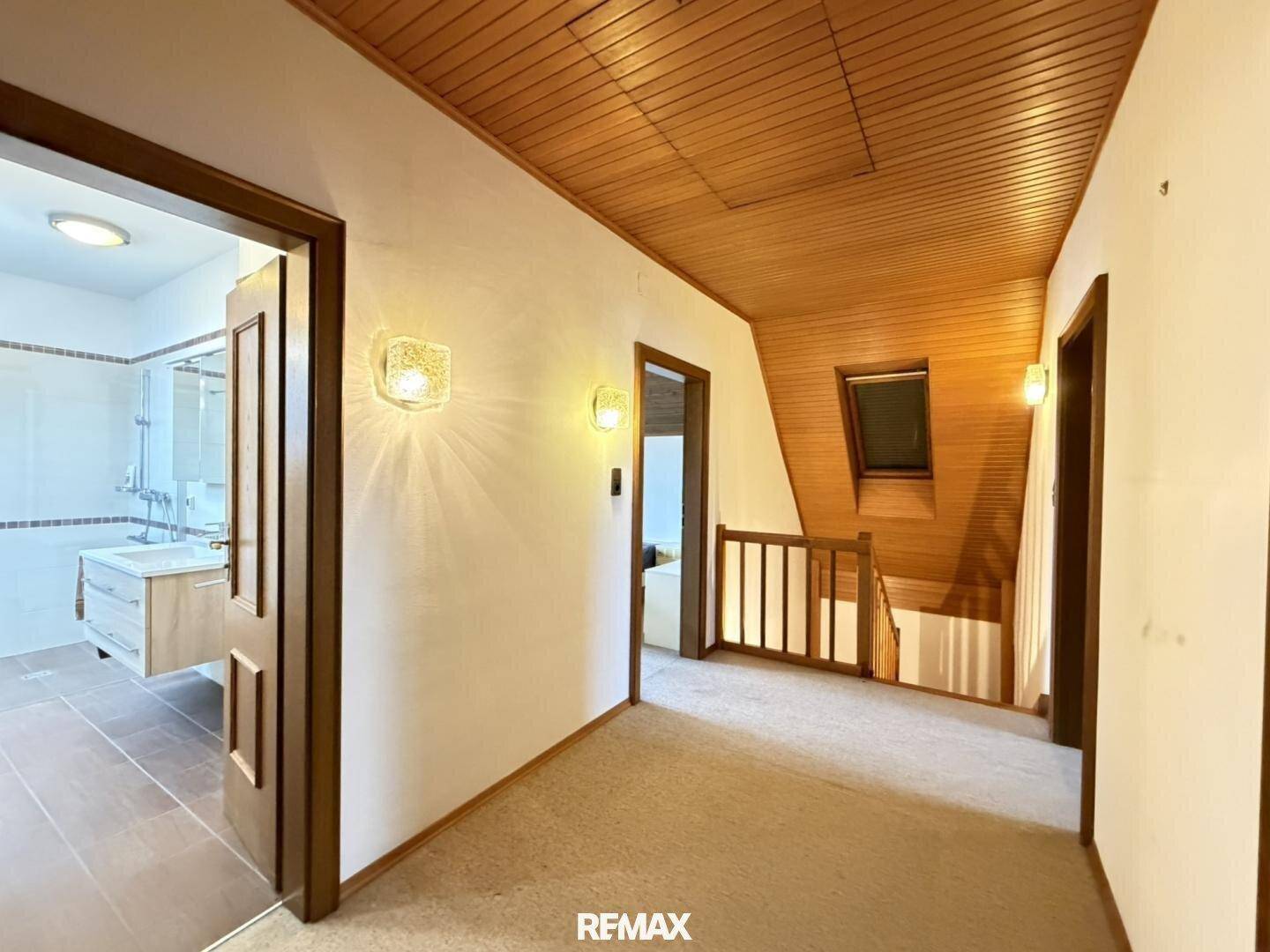 Heller Flur im Obergeschoss mit Teppichboden, Holzdecke und Dachfenster.