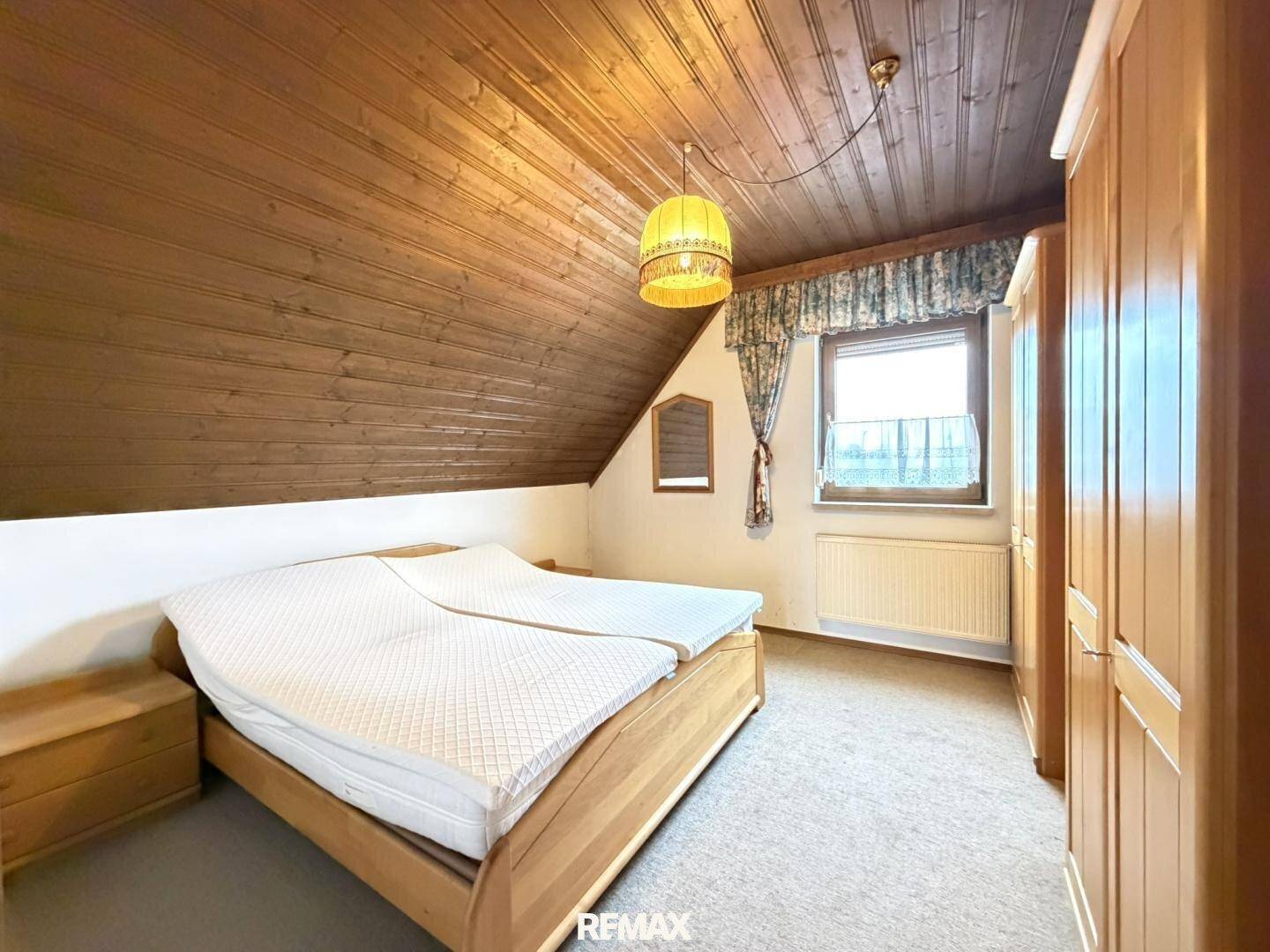 Schlafzimmer im Dachgeschoss mit Holzbalkendecke, Teppichboden und Doppelbett.