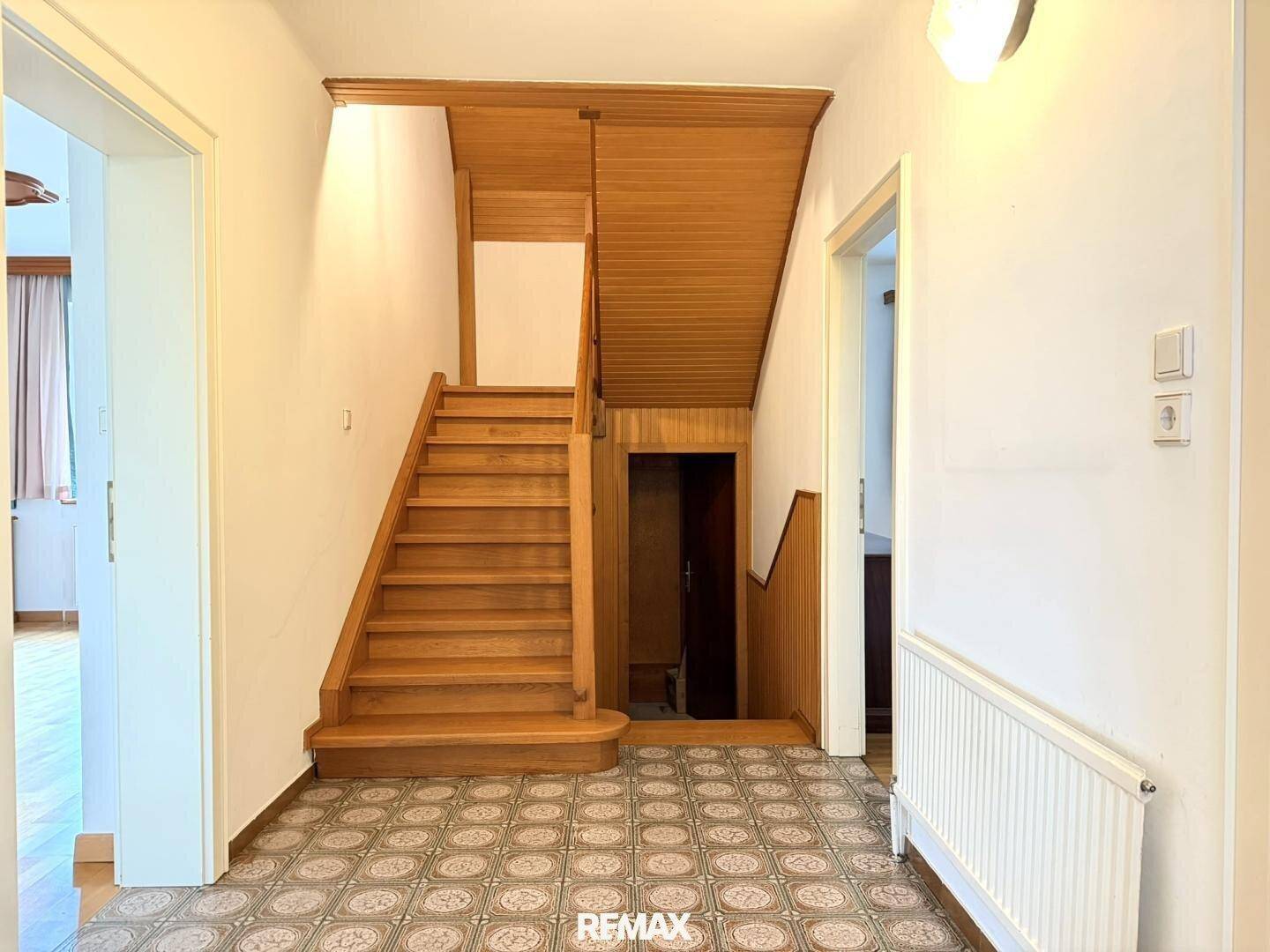 Heller Flur mit Holztreppe und gemusterten Fliesen, der zu den oberen Etagen führt.