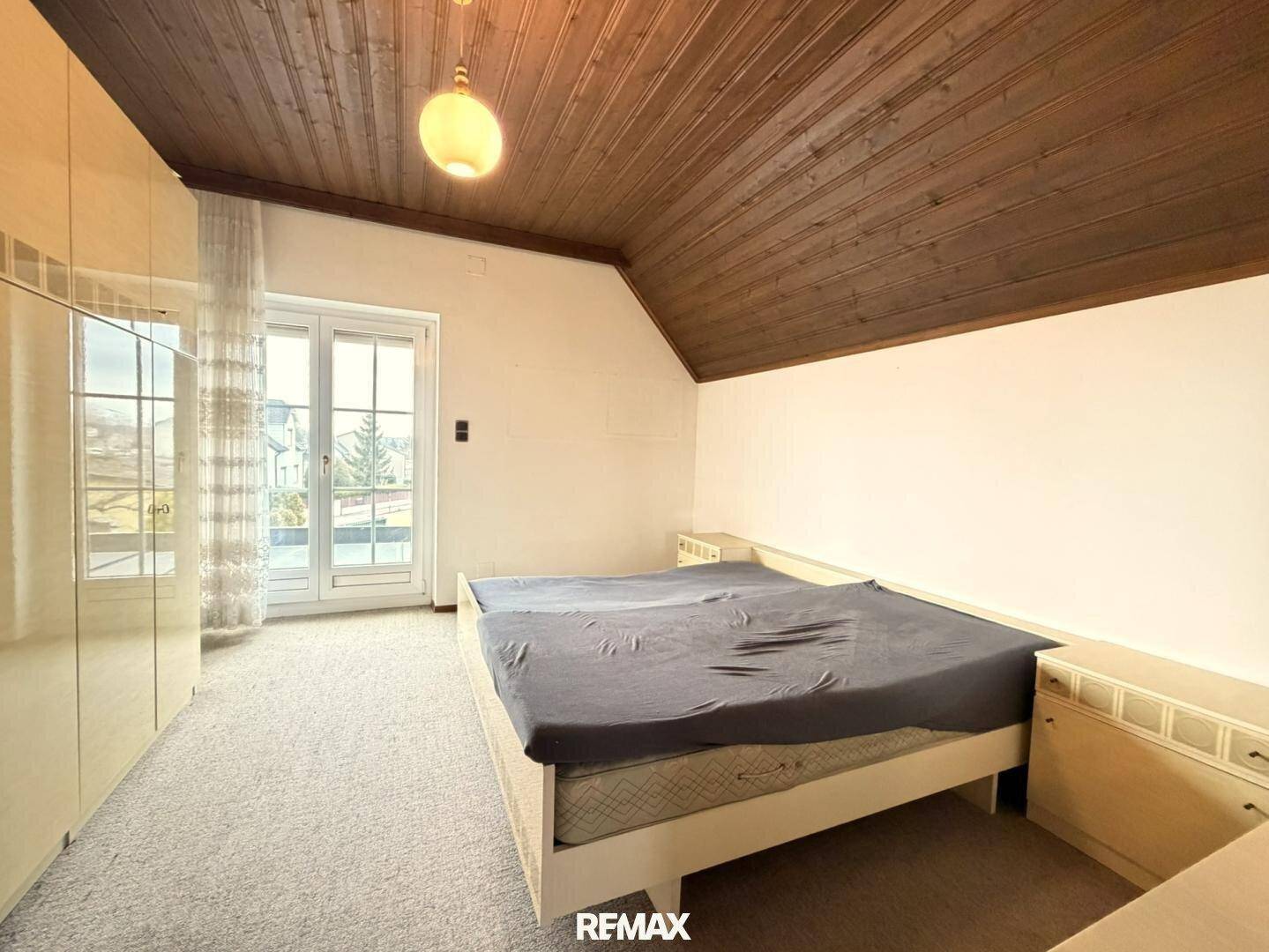 Schlafzimmer im Dachgeschoss mit Zugang zum Balkon, Teppichboden und Holzdecke.
