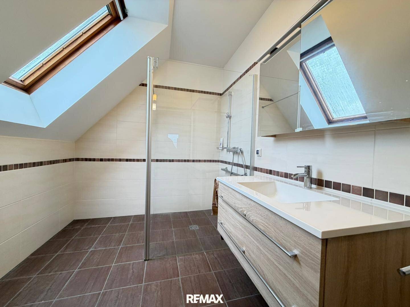 Modernes Badezimmer im Dachgeschoss mit Dusche, Waschtisch und Dachfenstern.