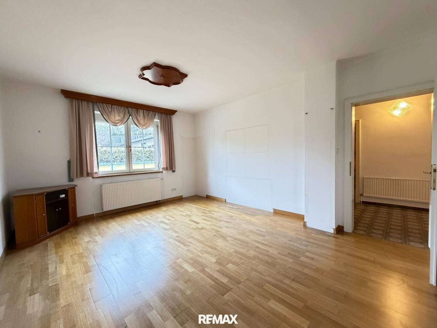 Helles Wohnzimmer mit Parkettboden, weiß gestrichenen Wänden und Fensterblick.